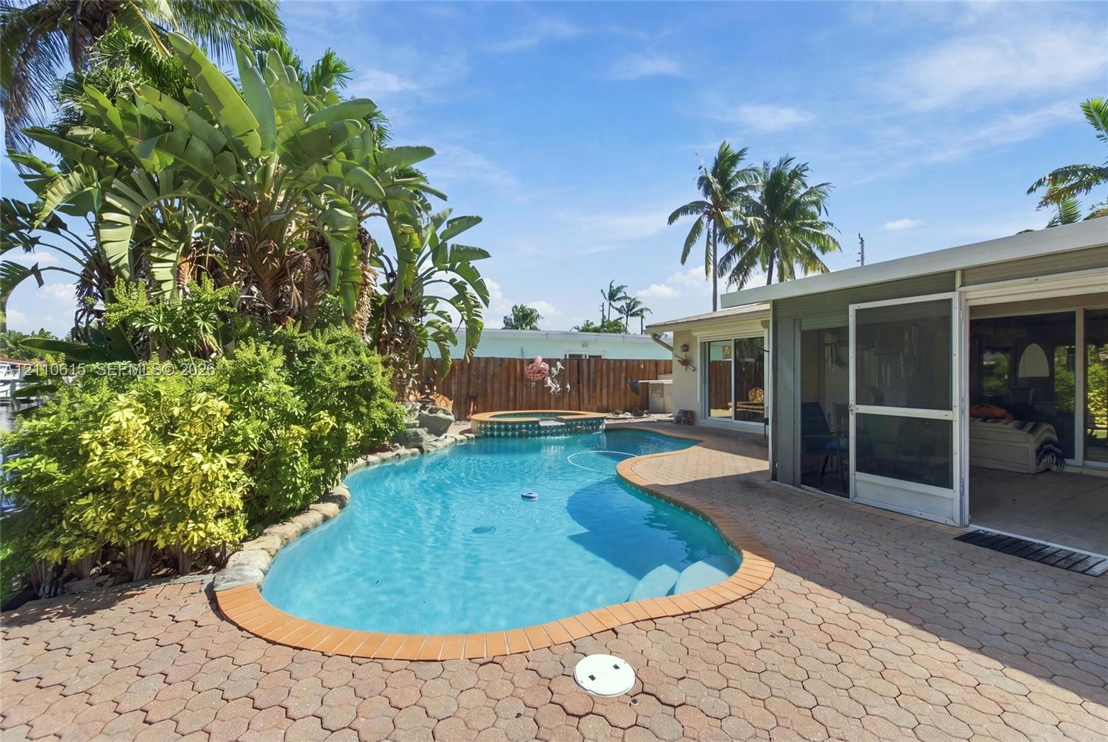 Freeform swimming pool with integrated spa, concrete paver patio, screened lanai, and wood perimeter fencing