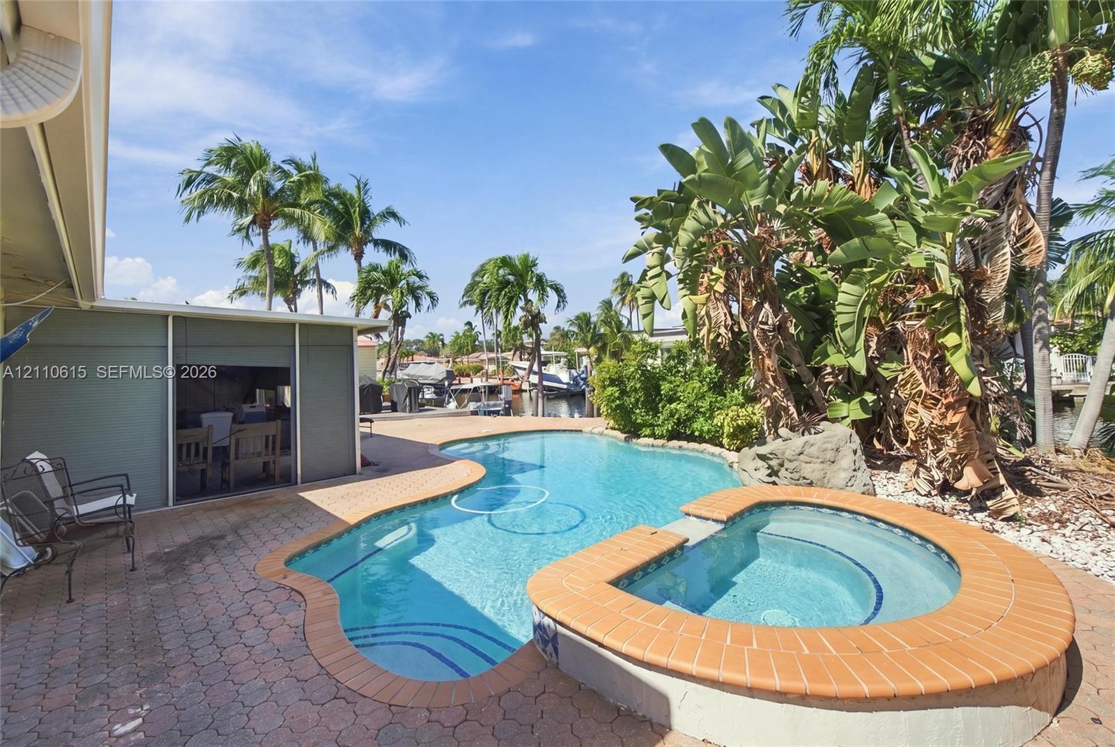 In-ground swimming pool with an integrated elevated spa, brick paver patio, and mature tropical landscaping