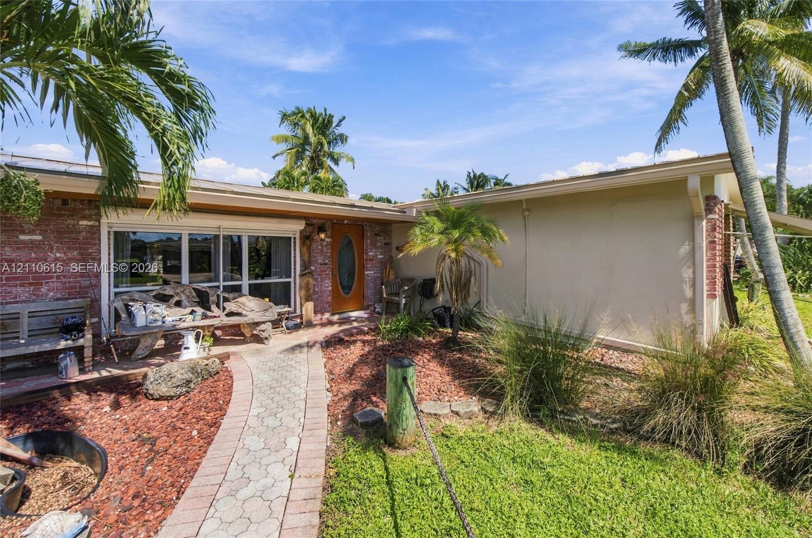 Single-story exterior featuring red brick masonry, stucco siding, an arched glass-panel front door, and a decorative concrete paver walkway
