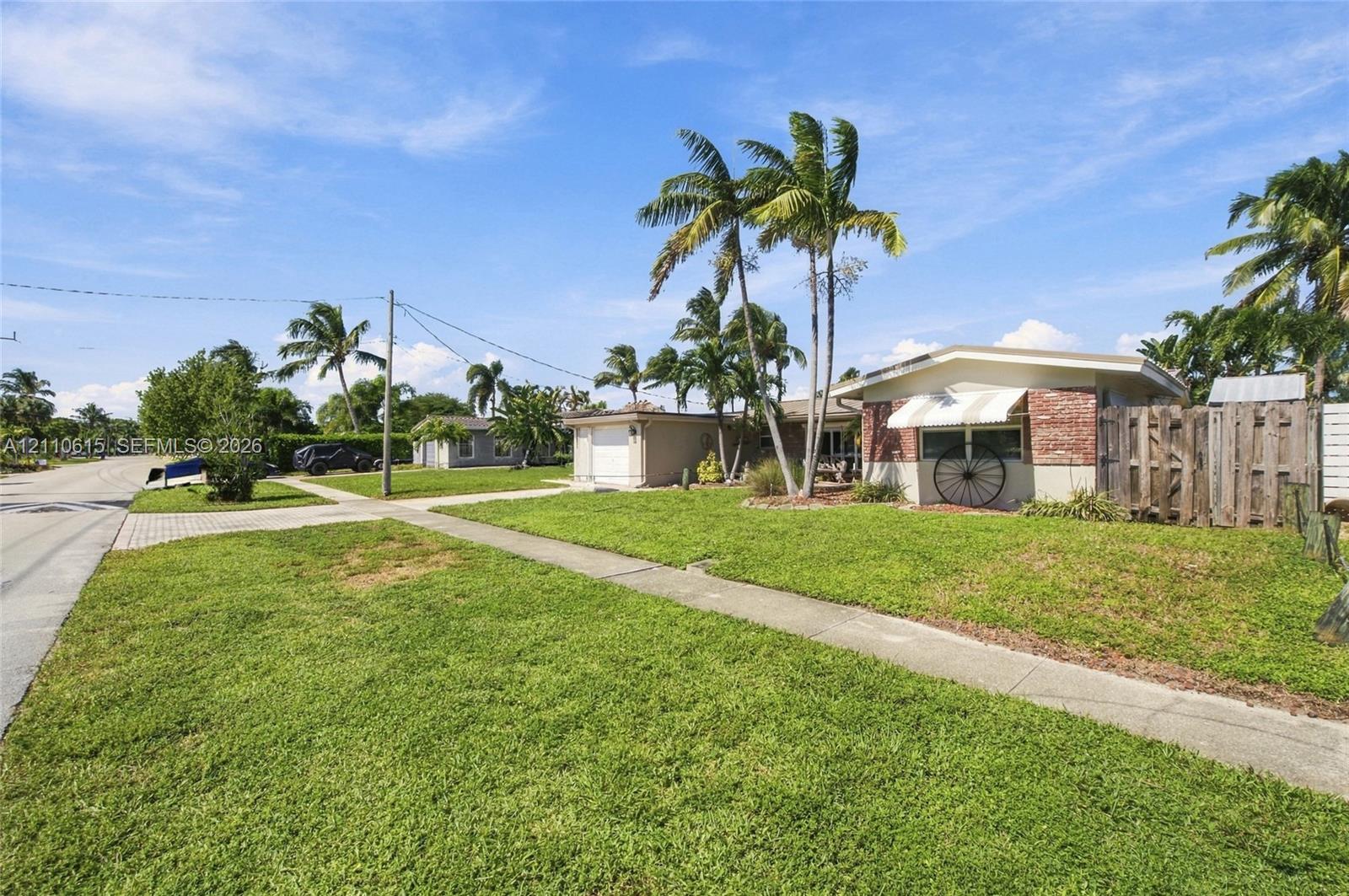Single-story residence featuring brick facade detailing, an attached garage, striped window awnings, and mature palm trees