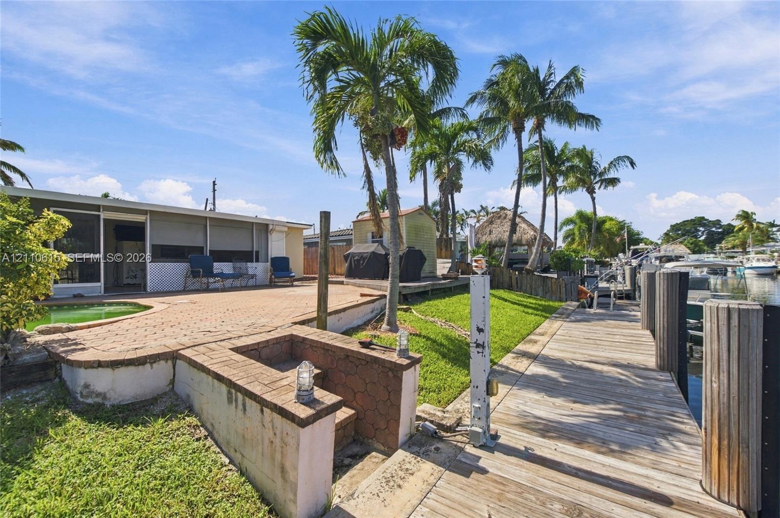 Waterfront property featuring a wooden dock, paver patio, in-ground pool, and mature palm trees