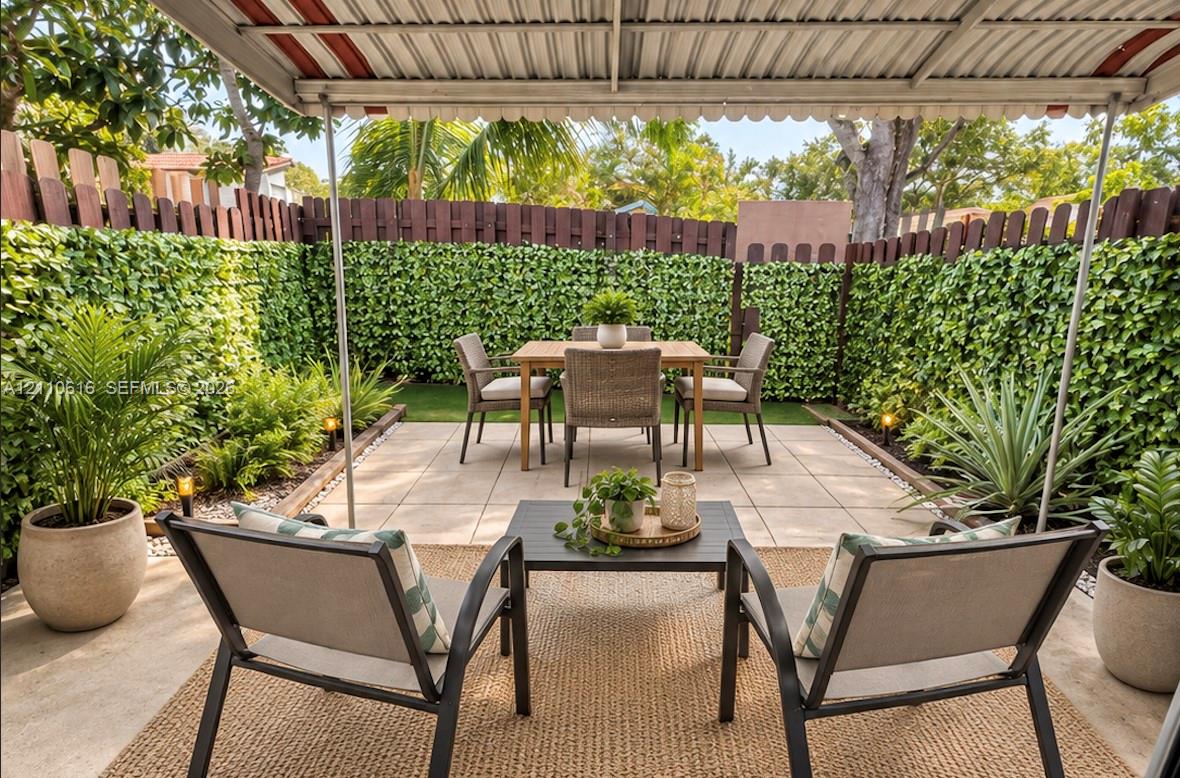 Covered patio featuring large-format concrete pavers, a privacy fence with integrated artificial greenery, and low-voltage landscape lighting Covered patio featuring large-format concrete pavers, a privacy fence with integrated artificial greenery, and low-voltage landscape lighting
