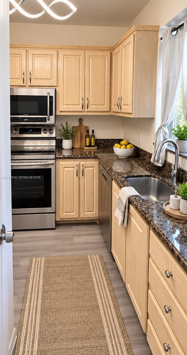 Kitchen featuring light-tone wood cabinetry, stone countertops, stainless steel appliances, wood-finish flooring, and a single-basin stainless steel sink with a high-arch faucet Kitchen featuring light-tone wood cabinetry, stone countertops, stainless steel appliances, wood-finish flooring, and a single-basin stainless steel sink with a high-arch faucet