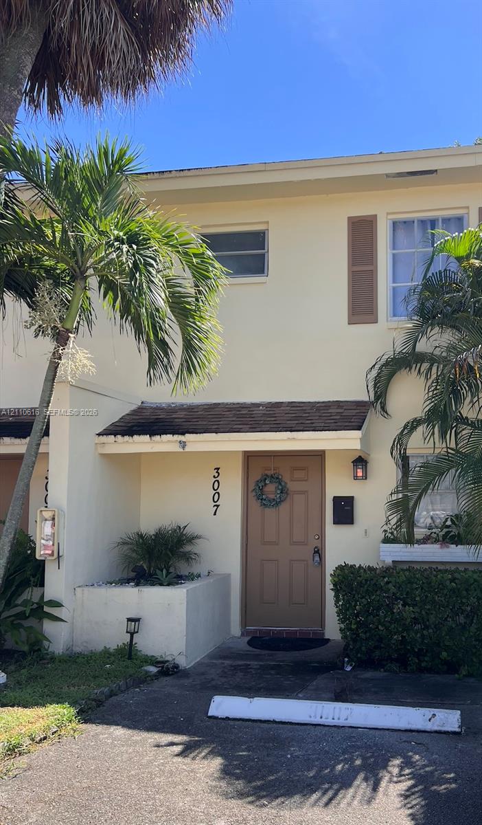 Two-story exterior featuring a light-toned facade, decorative window shutters, a covered entryway, and a built-in concrete planter Two-story exterior featuring a light-toned facade, decorative window shutters, a covered entryway, and a built-in concrete planter