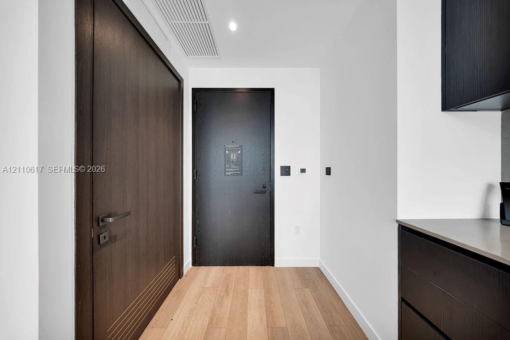 Entryway featuring wood-finish flooring, a matte black door, a full-height dark wood door with horizontal detailing, and modern flat-panel dark cabinetry with a solid surface countertop
