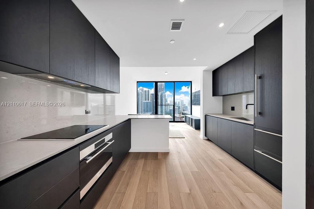 Modern kitchen featuring matte black cabinetry, light-toned stone countertops, built-in stainless steel appliances, wood-finish flooring, and recessed lighting Modern kitchen featuring matte black cabinetry, light-toned stone countertops, built-in stainless steel appliances, wood-finish flooring, and recessed lighting