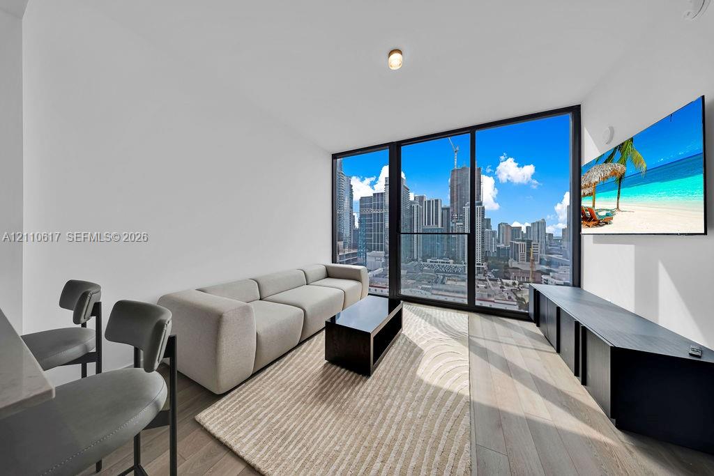 Floor-to-ceiling windows featuring urban skyline scenery, wood-finish flooring, and a sleek matte black built-in media console