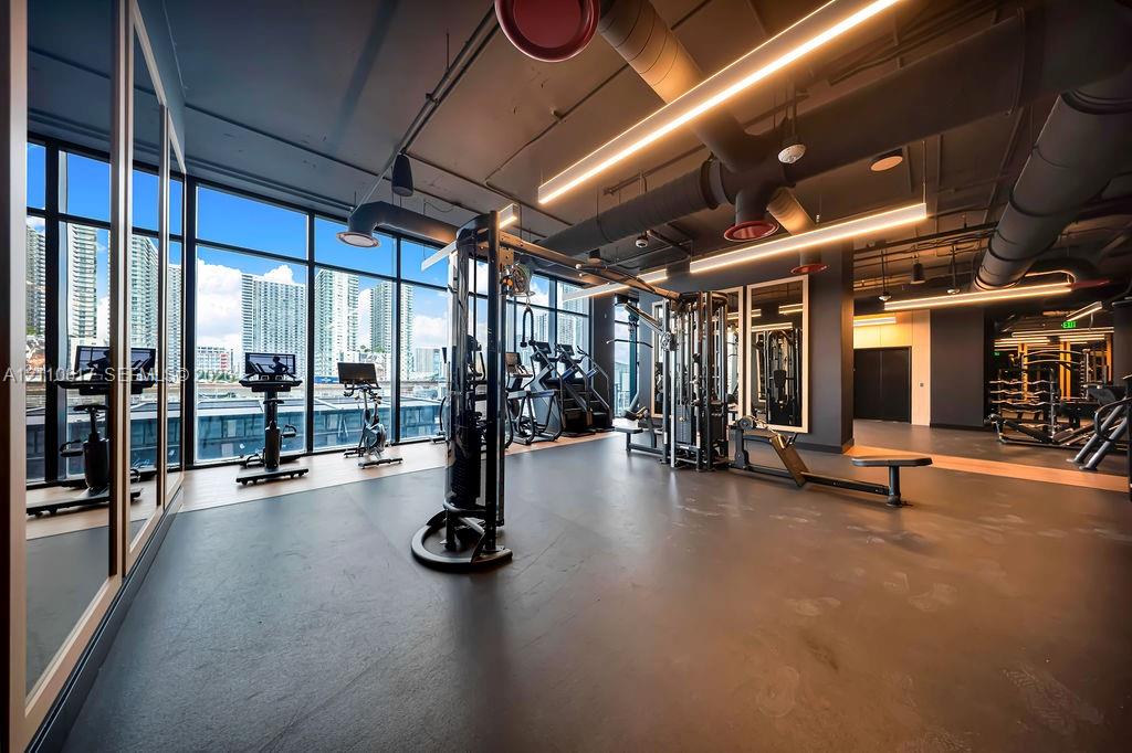 Fitness center featuring floor-to-ceiling windows, industrial-style exposed ductwork, recessed linear lighting, and wall-to-wall mirrors