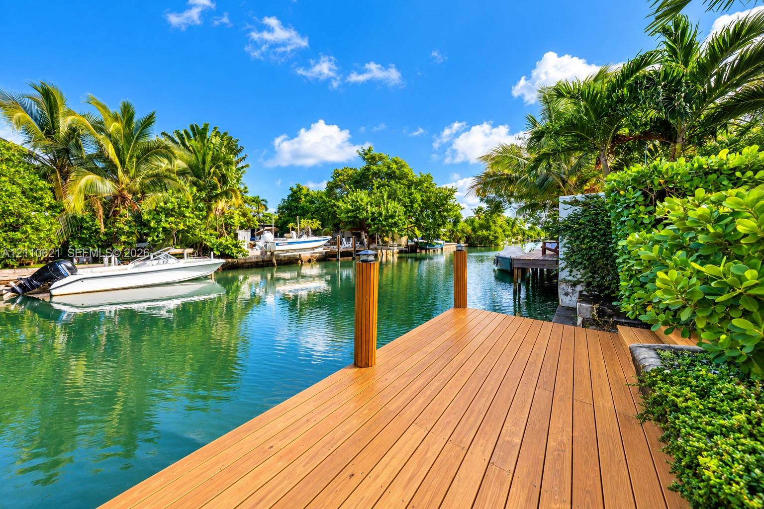 Waterfront dock featuring composite decking, wooden pilings with solar caps, and mature tropical landscaping Waterfront dock featuring composite decking, wooden pilings with solar caps, and mature tropical landscaping