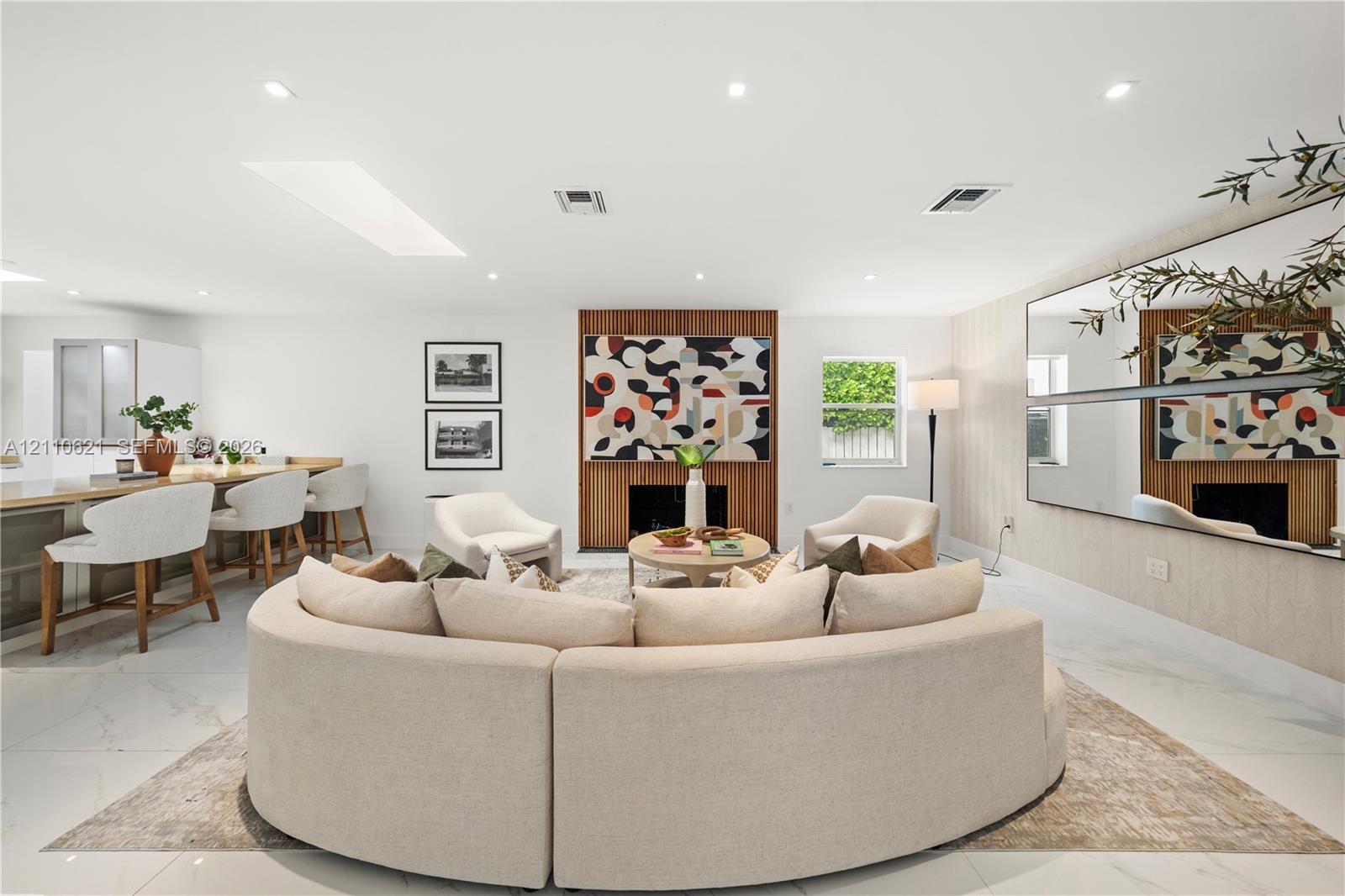 Open-concept living space featuring large-format tile flooring, a recessed skylight, recessed lighting, a wood-paneled fireplace surround, and extensive wall-mounted mirrors