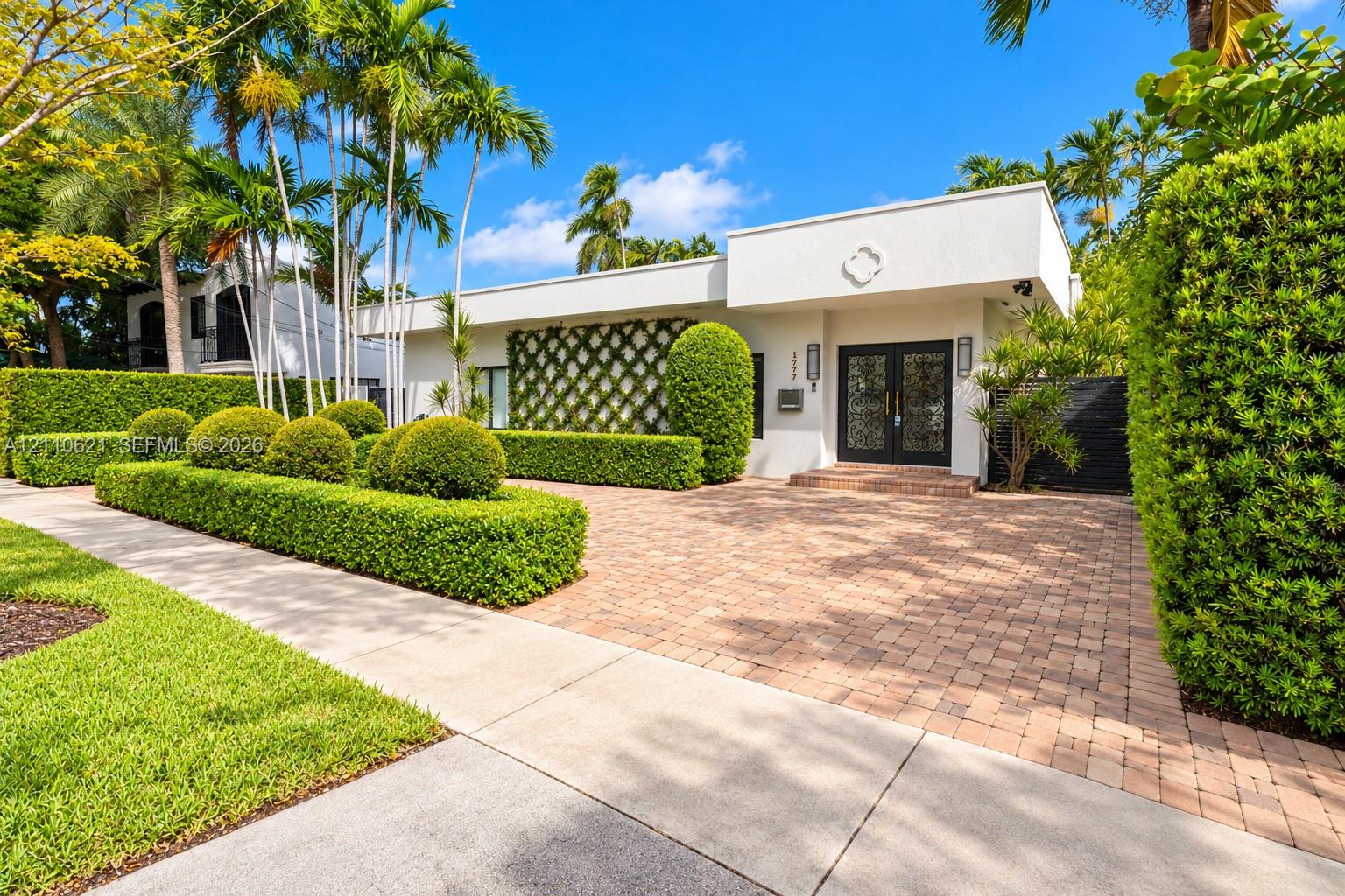 Modern stucco exterior featuring a patterned wall trellis, paver driveway, double glass-paneled entry doors, and professional landscaping Modern stucco exterior featuring a patterned wall trellis, paver driveway, double glass-paneled entry doors, and professional landscaping