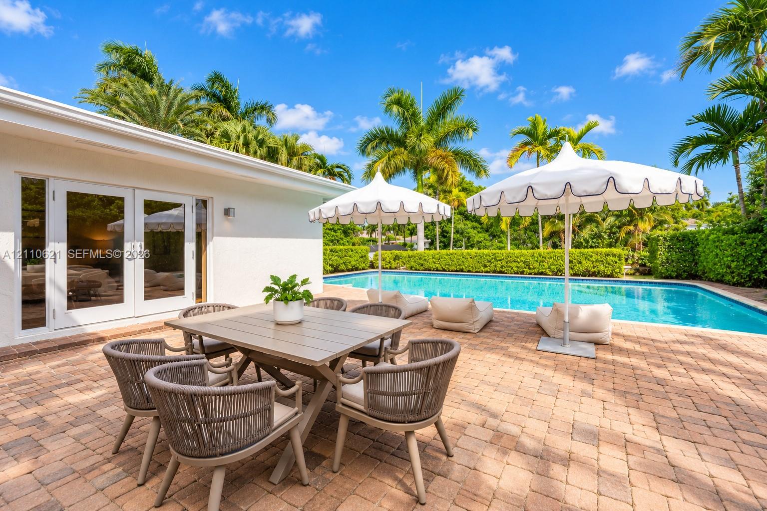 Backyard patio featuring paver hardscaping, a swimming pool, and mature palm trees enclosed by manicured hedges Backyard patio featuring paver hardscaping, a swimming pool, and mature palm trees enclosed by manicured hedges