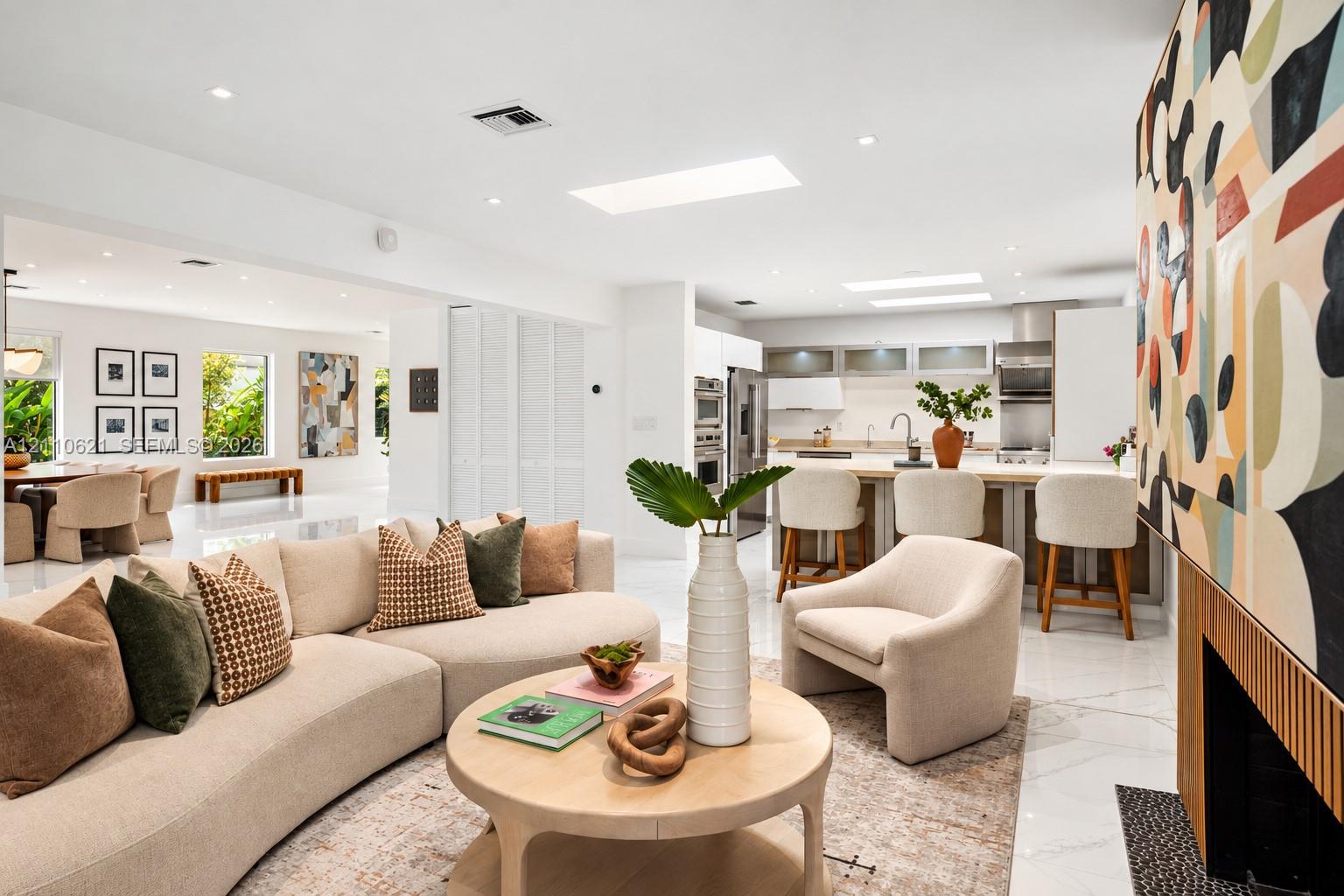 Open-concept living space featuring high ceilings with integrated skylights, polished stone-finish flooring, and a fireplace with wood-slat detailing