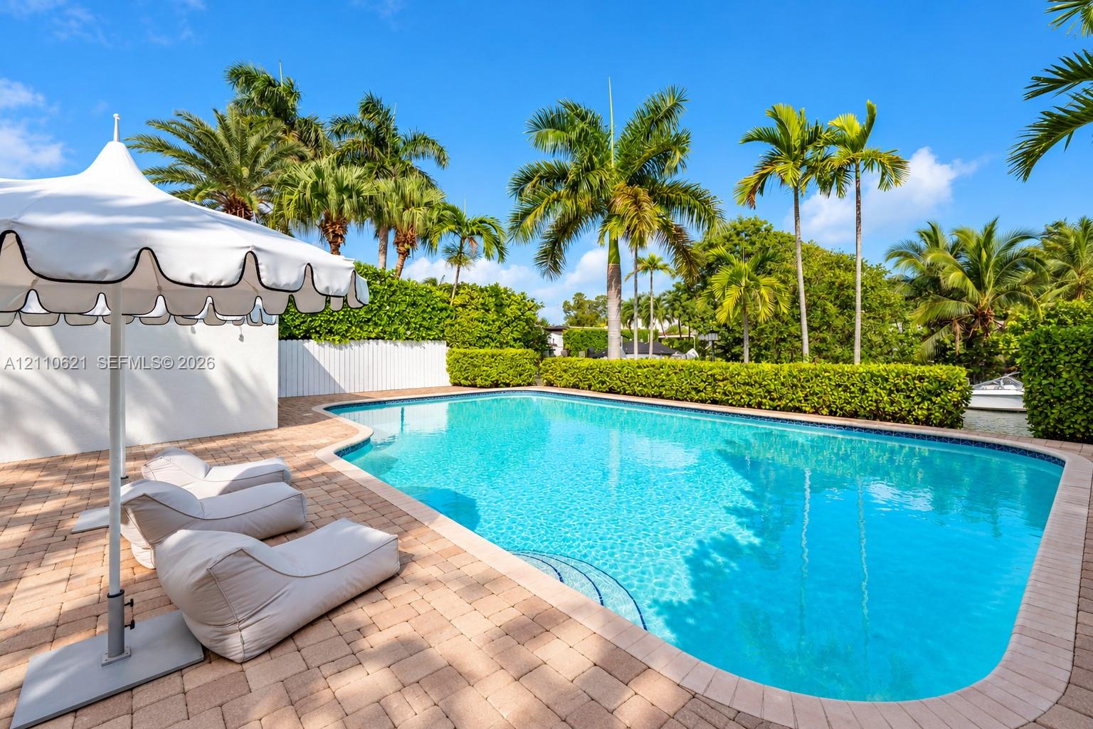 In-ground swimming pool featuring a brick-paver patio, perimeter privacy hedging, and mature palm trees In-ground swimming pool featuring a brick-paver patio, perimeter privacy hedging, and mature palm trees