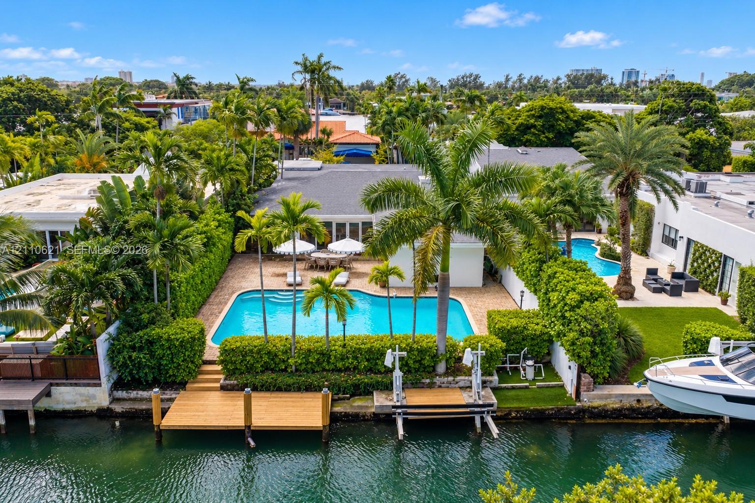 Waterfront property featuring a private swimming pool, a wood-finish dock, a boat lift, and lush landscaping Waterfront property featuring a private swimming pool, a wood-finish dock, a boat lift, and lush landscaping