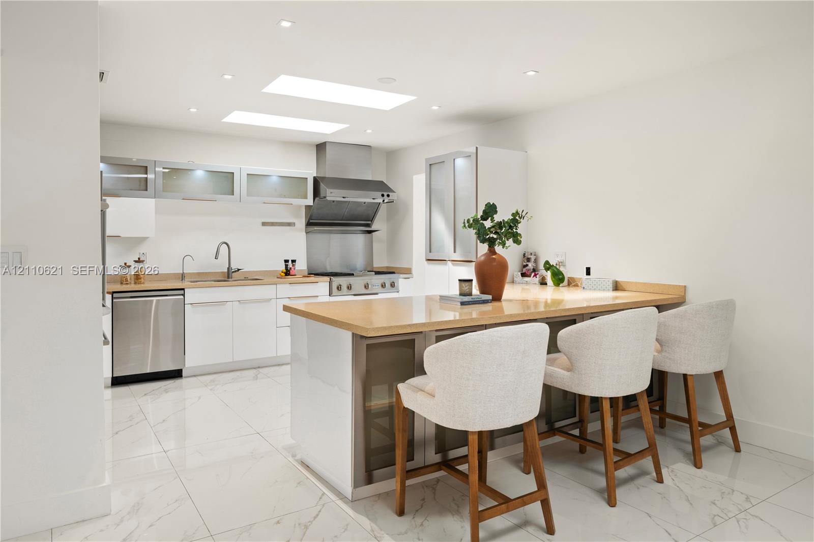 Kitchen featuring white flat-panel cabinetry, stainless steel appliances, solid surface countertops, a central island with integrated storage, and recessed ceiling lighting