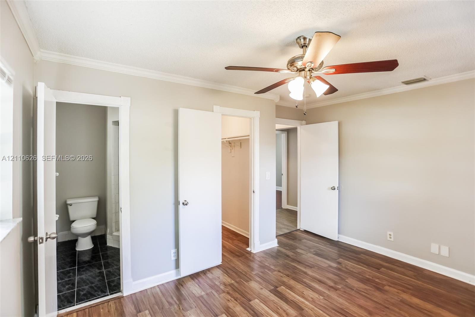Wood-finish flooring, ceiling fan with integrated light fixture, crown molding, and two interior doorways with built-in storage