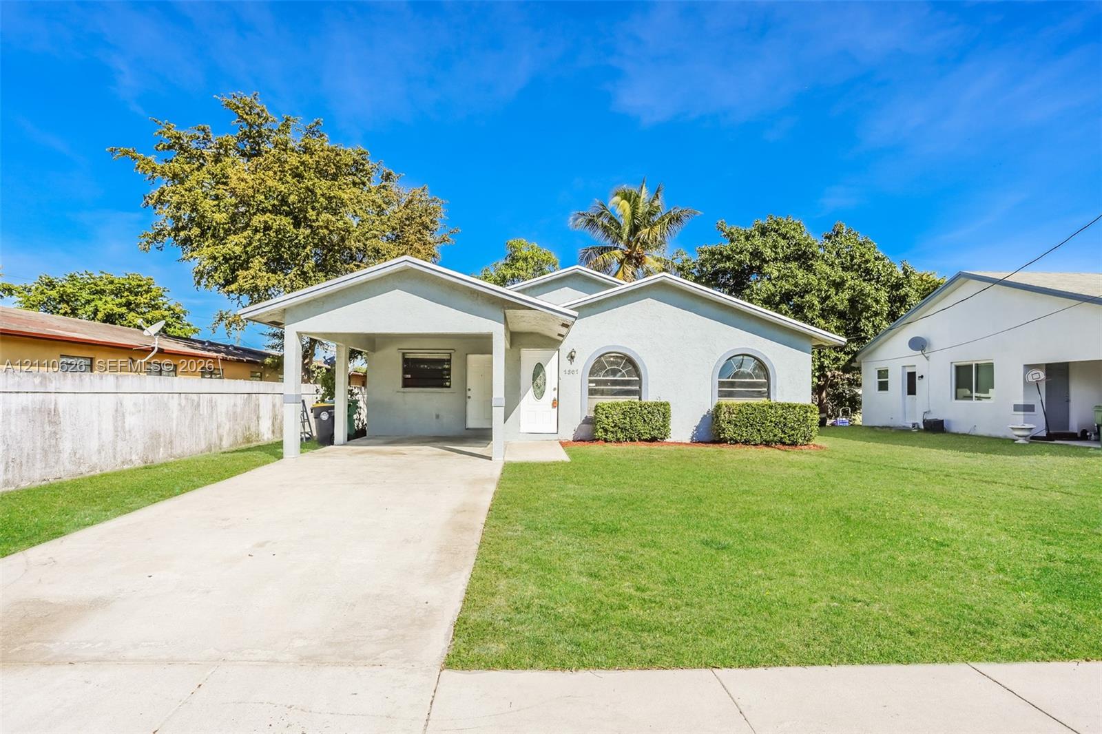 Single-story exterior featuring a light-toned stucco facade, arched windows, covered carport, and a manicured front lawn