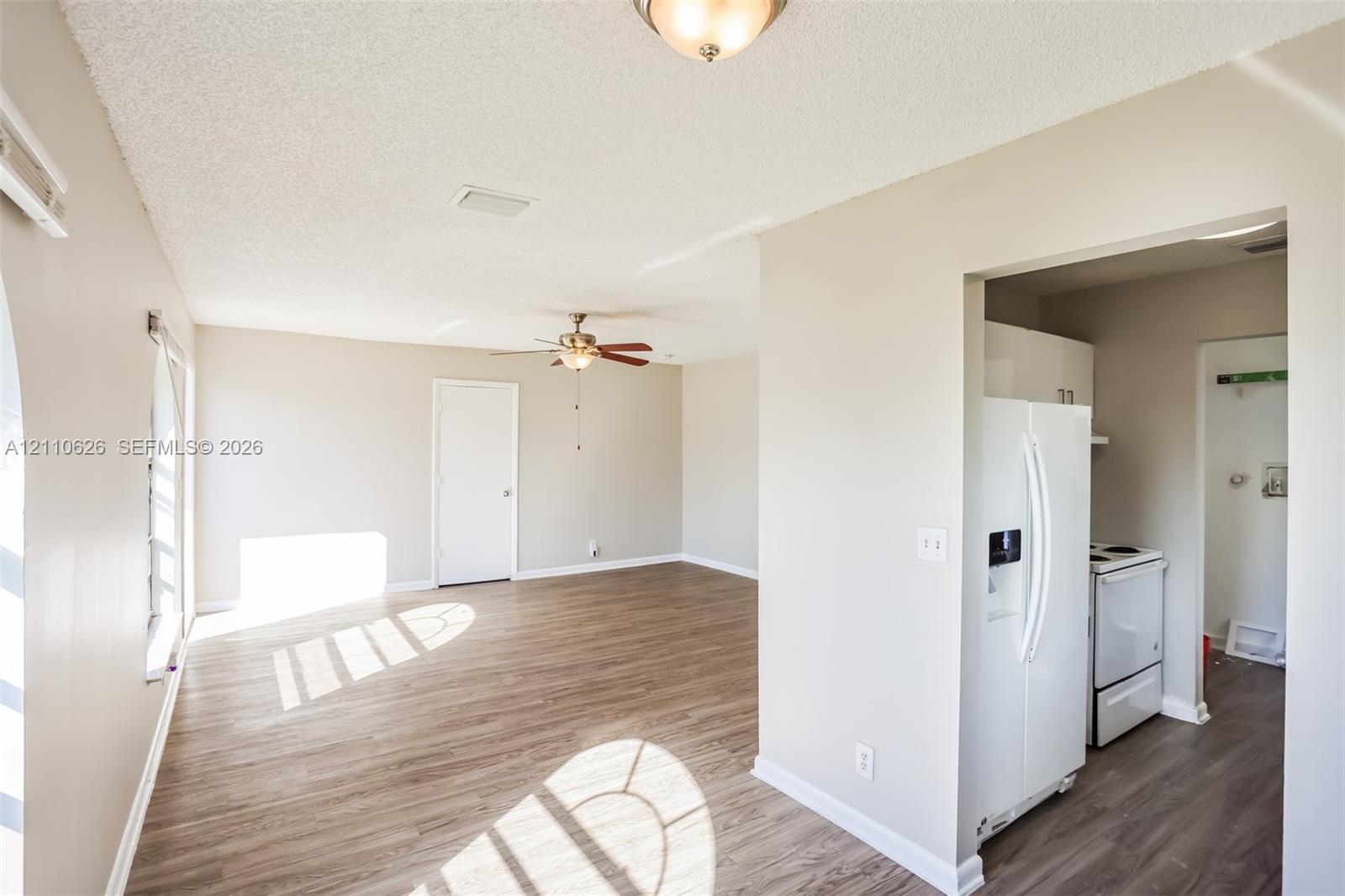 Wood-finish flooring, neutral wall tones, ceiling fan with integrated lighting, and kitchen equipped with a white refrigerator and electric range