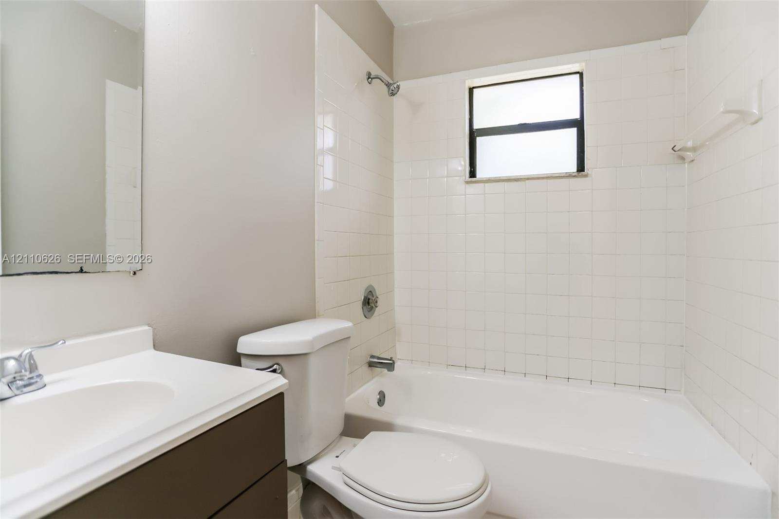 Bathroom featuring a white bathtub, white wall tiling, single-basin vanity with a white countertop, and a built-in window