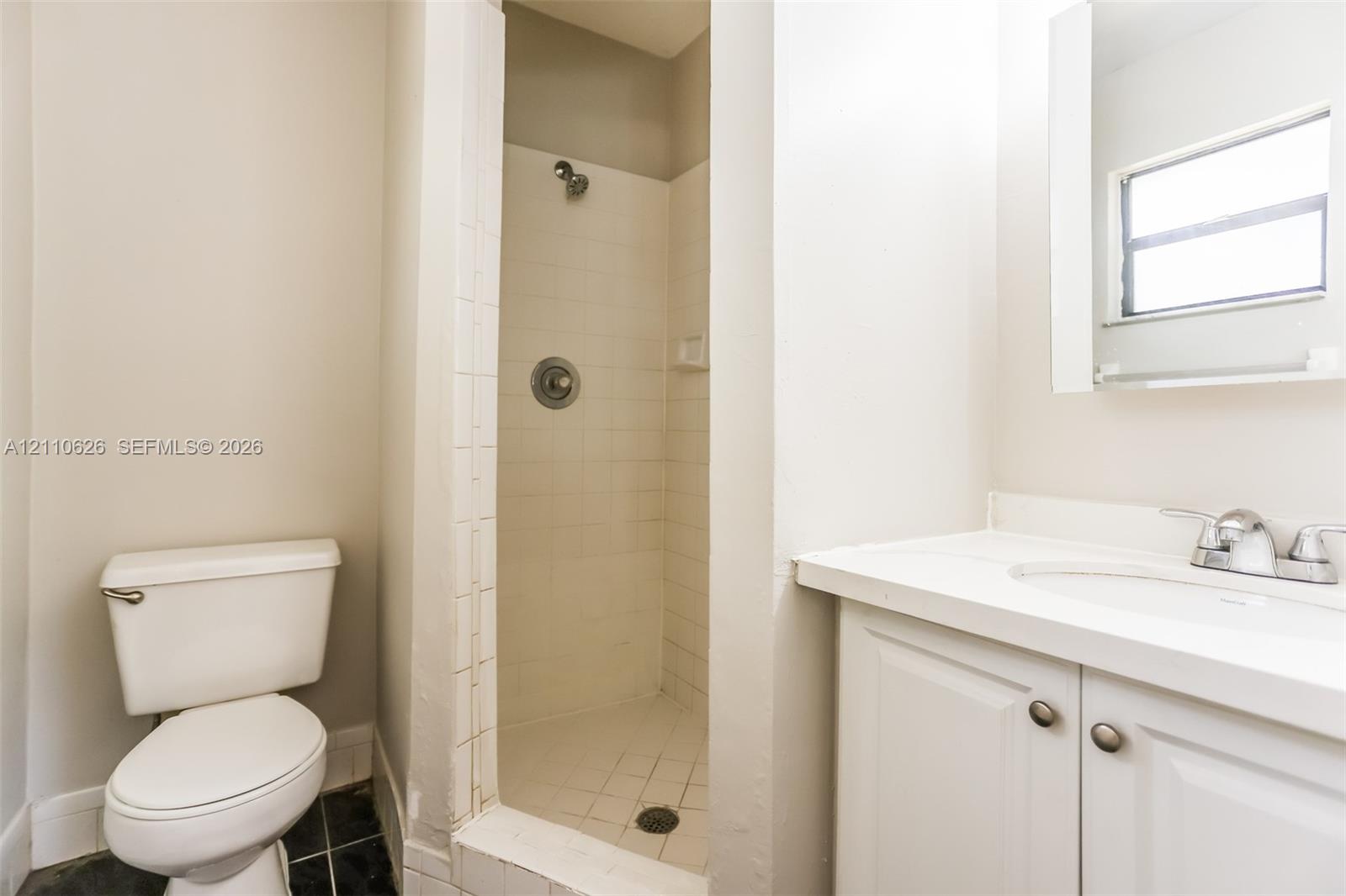 Bathroom featuring a white vanity with an integrated sink, polished chrome faucet, tile-surround shower, and a window