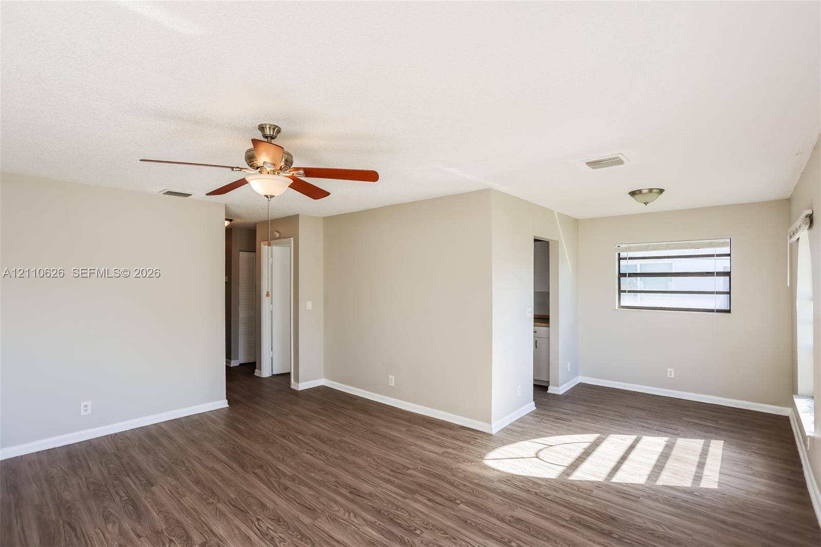 Neutral-toned interior space featuring wood-finish flooring, a ceiling fan with integrated lighting, and horizontal slatted windows