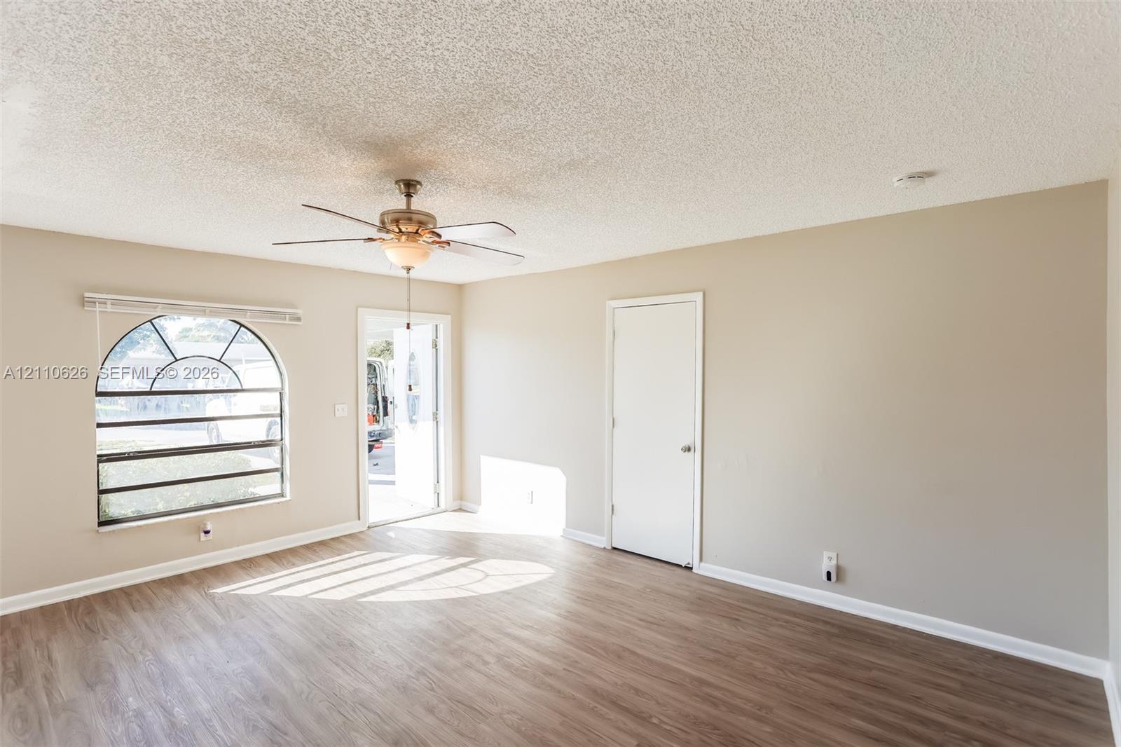 Interior space featuring wood-finish flooring, an arched window, a ceiling fan with light fixture, and neutral-toned walls