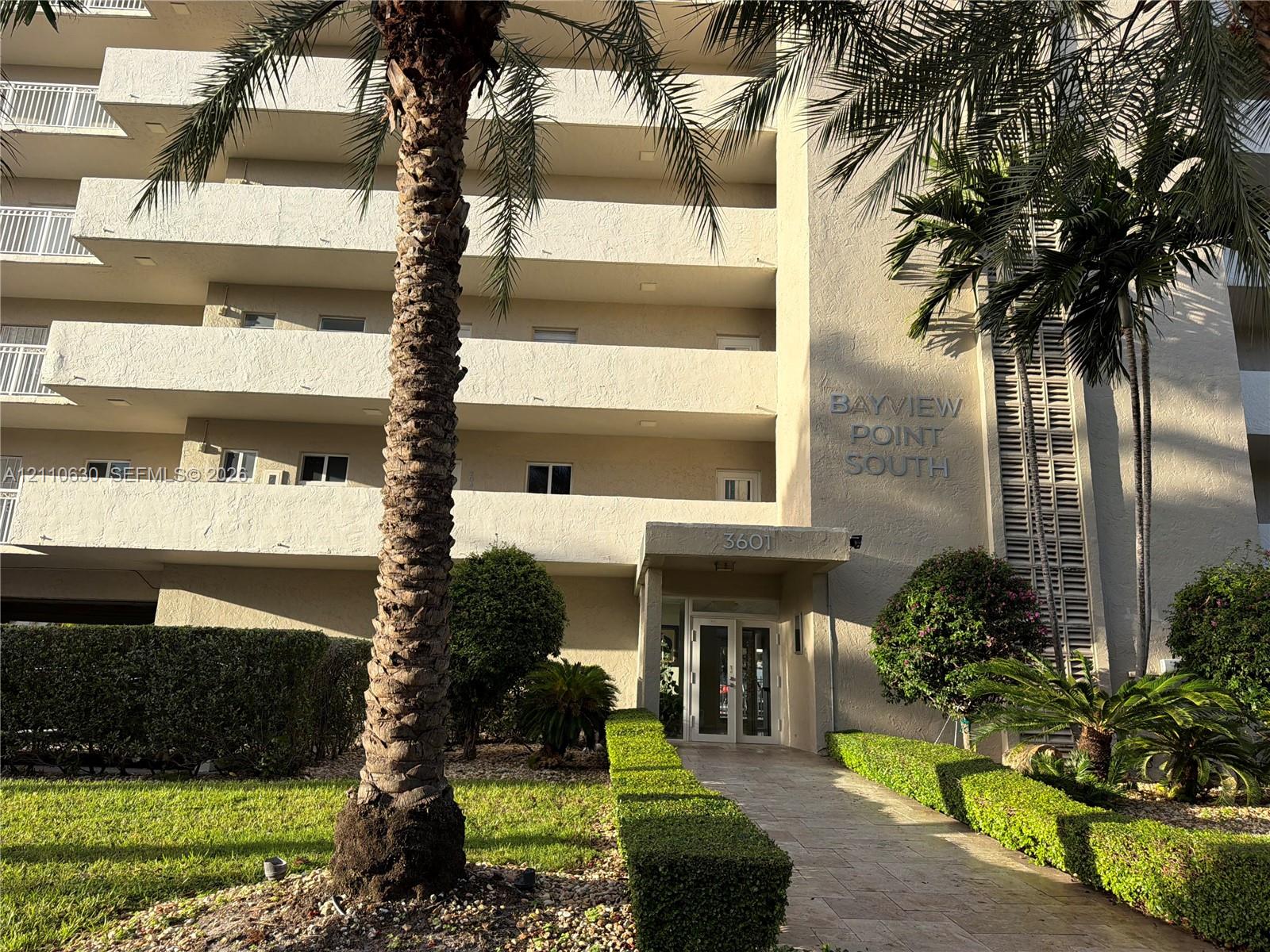 Multi-story stucco exterior featuring private recessed balconies, a covered entryway, and mature palm tree landscaping Multi-story stucco exterior featuring private recessed balconies, a covered entryway, and mature palm tree landscaping