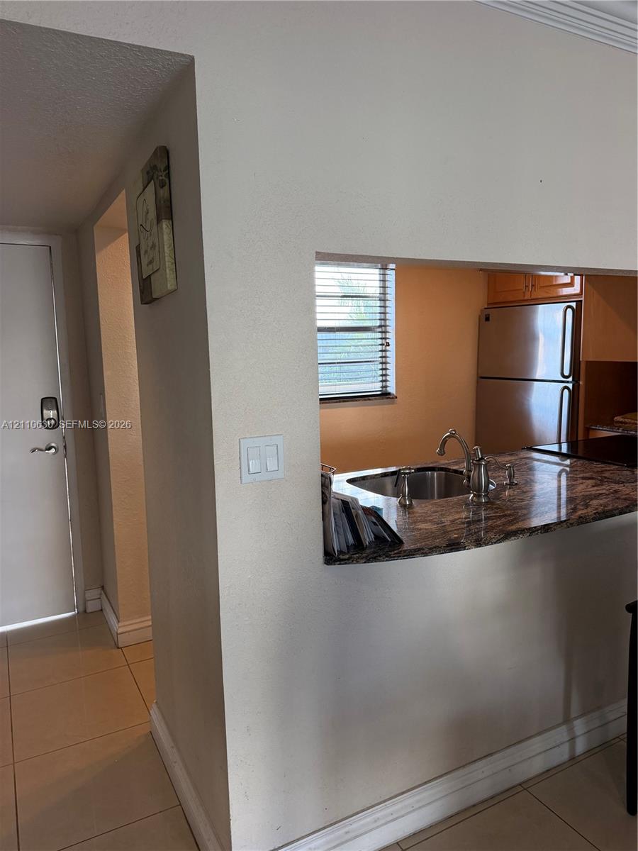 Kitchen pass-through featuring a stone-surface countertop, stainless steel sink with a high-arch faucet, and tile flooring Kitchen pass-through featuring a stone-surface countertop, stainless steel sink with a high-arch faucet, and tile flooring