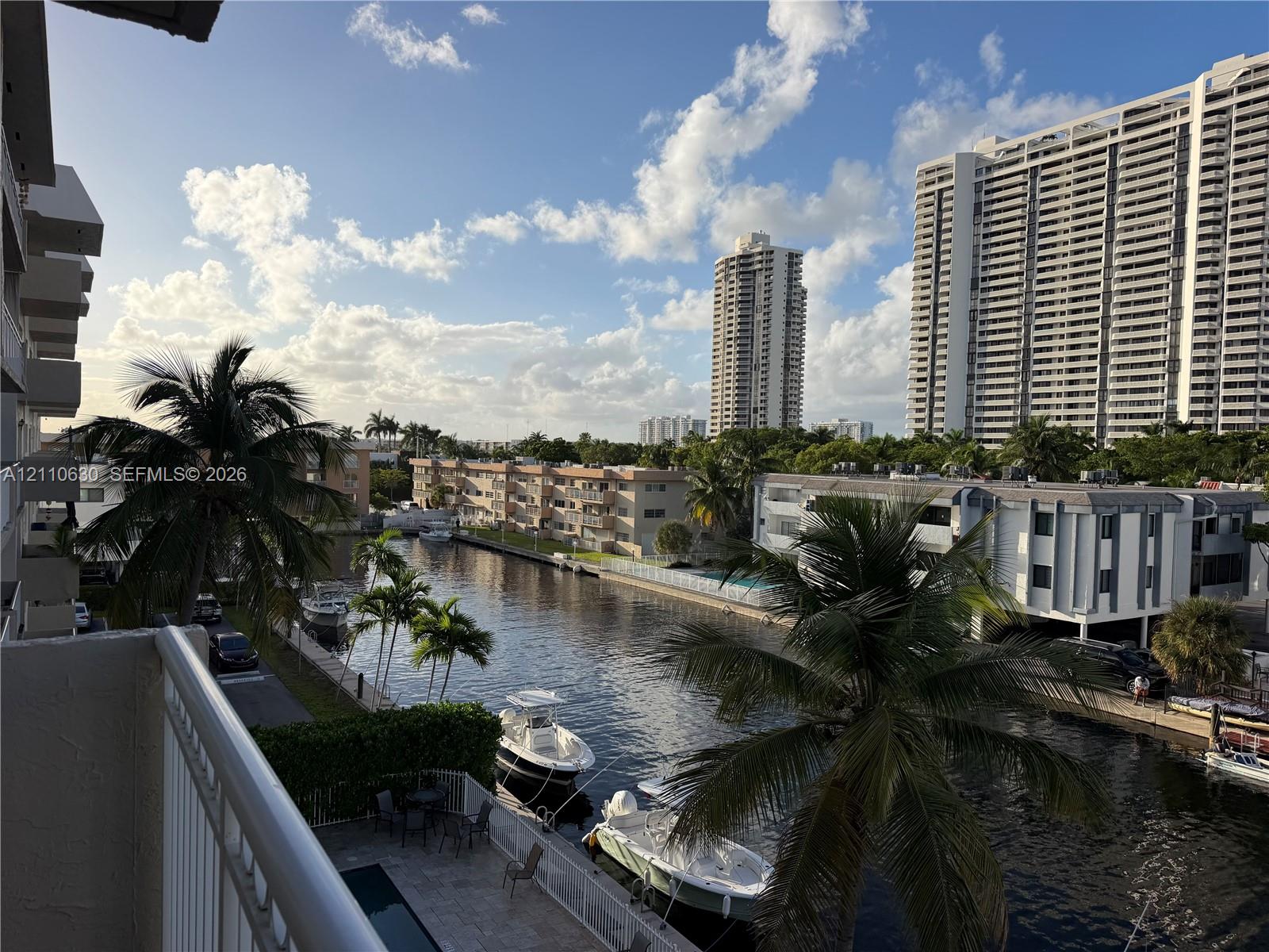 Elevated balcony with a metal railing overlooking a canal, featuring tropical palm trees and direct water access