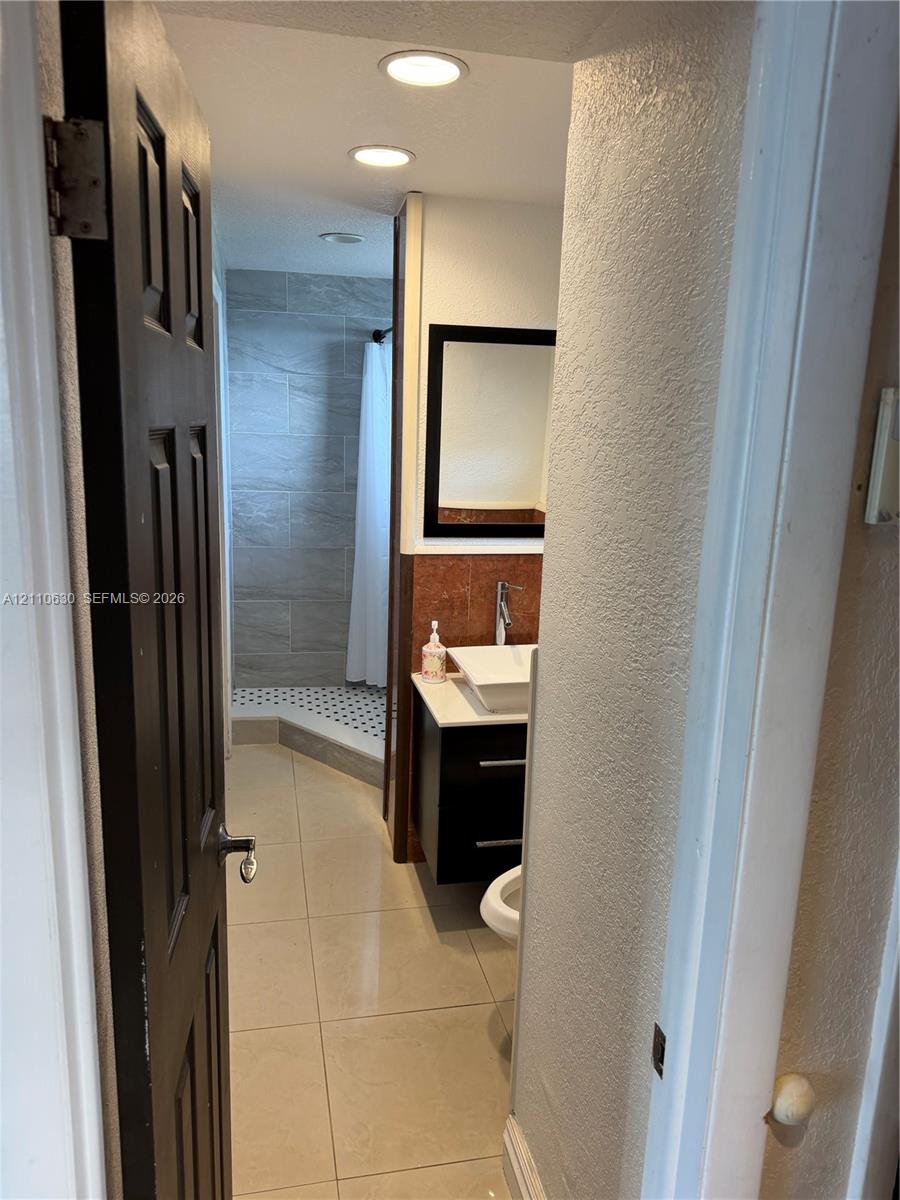 Bathroom featuring large-format floor tiling, a floating vanity with a rectangular vessel sink, integrated recessed lighting, and a walk-in shower with stone-style wall tile and geometric floor tile