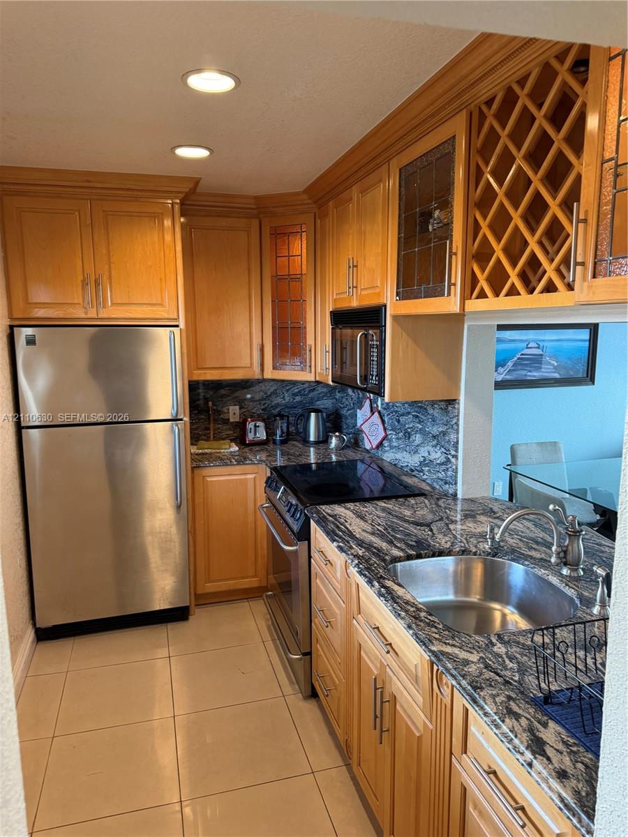 Kitchen featuring wood cabinetry with built-in wine storage, natural stone countertops, stainless steel appliances, and tile flooring Kitchen featuring wood cabinetry with built-in wine storage, natural stone countertops, stainless steel appliances, and tile flooring