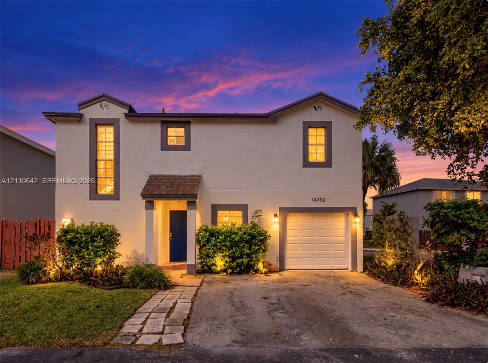 Two-story exterior featuring light-toned stucco, a single-car garage, a covered entryway, and vertical accent windows