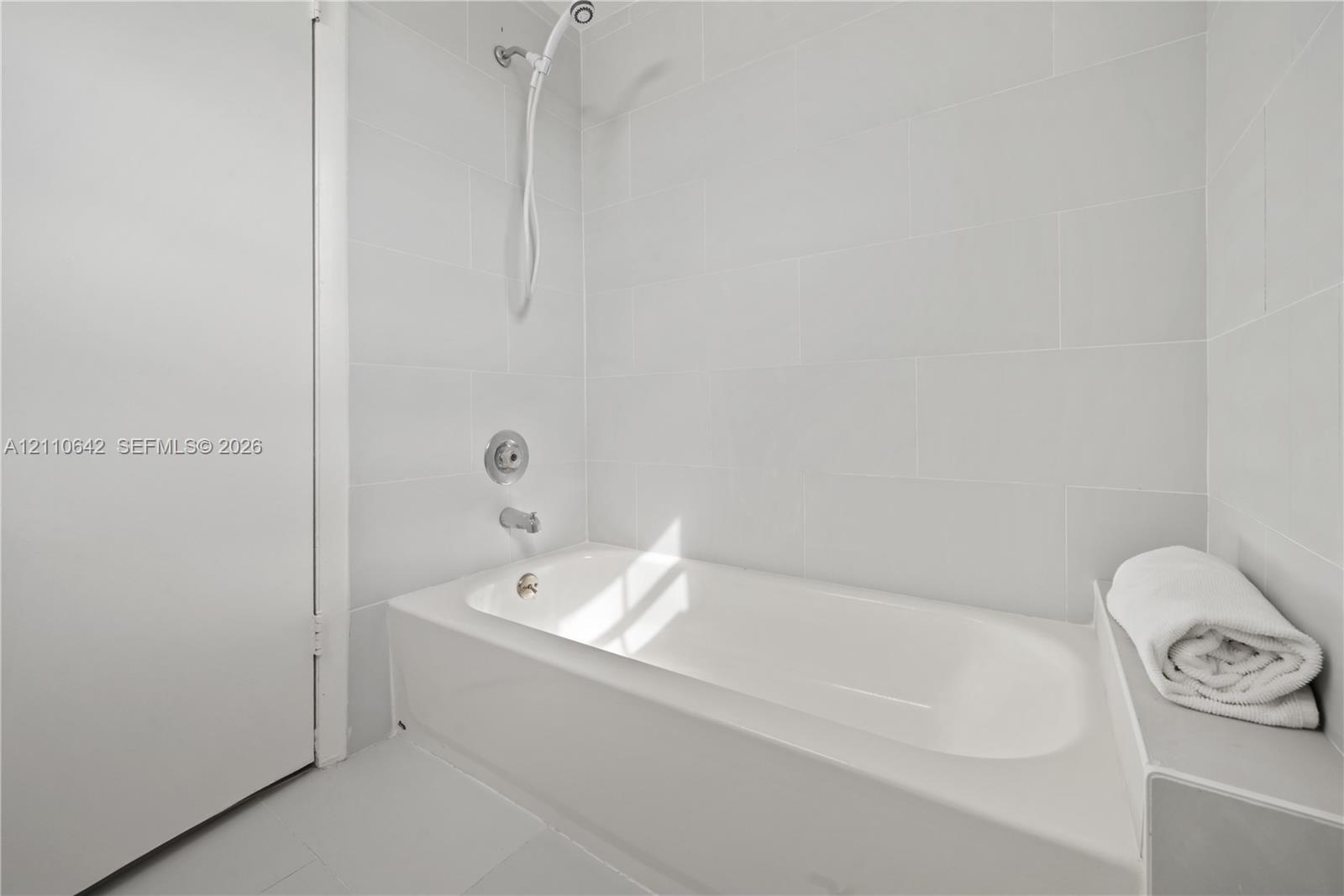 Full-size soaking tub featuring a wall-mounted shower head, polished chrome fixtures, and white tile surround