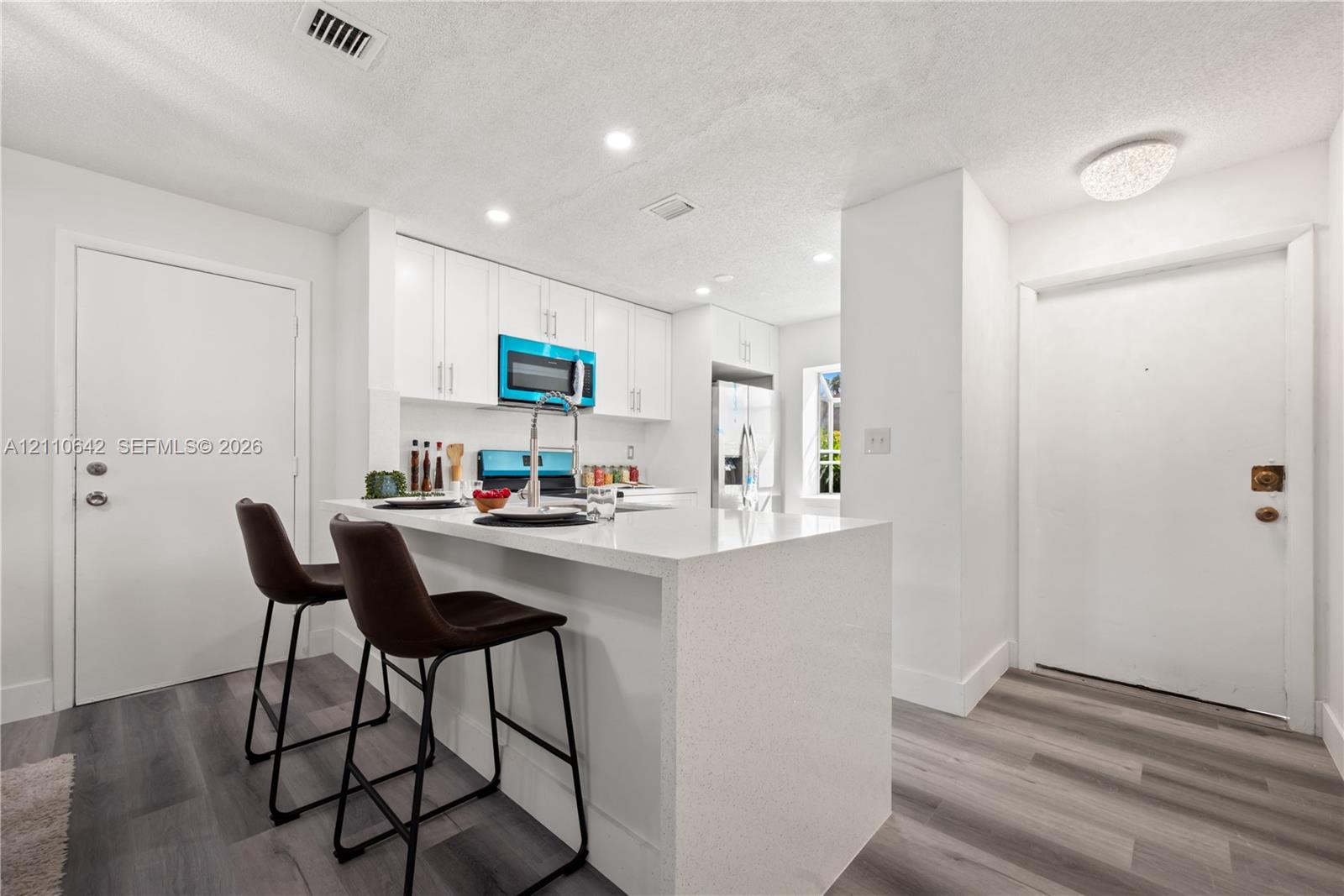 Kitchen featuring white cabinetry, stone-surface breakfast bar with waterfall edge, wood-finish flooring, and stainless steel appliances Kitchen featuring white cabinetry, stone-surface breakfast bar with waterfall edge, wood-finish flooring, and stainless steel appliances