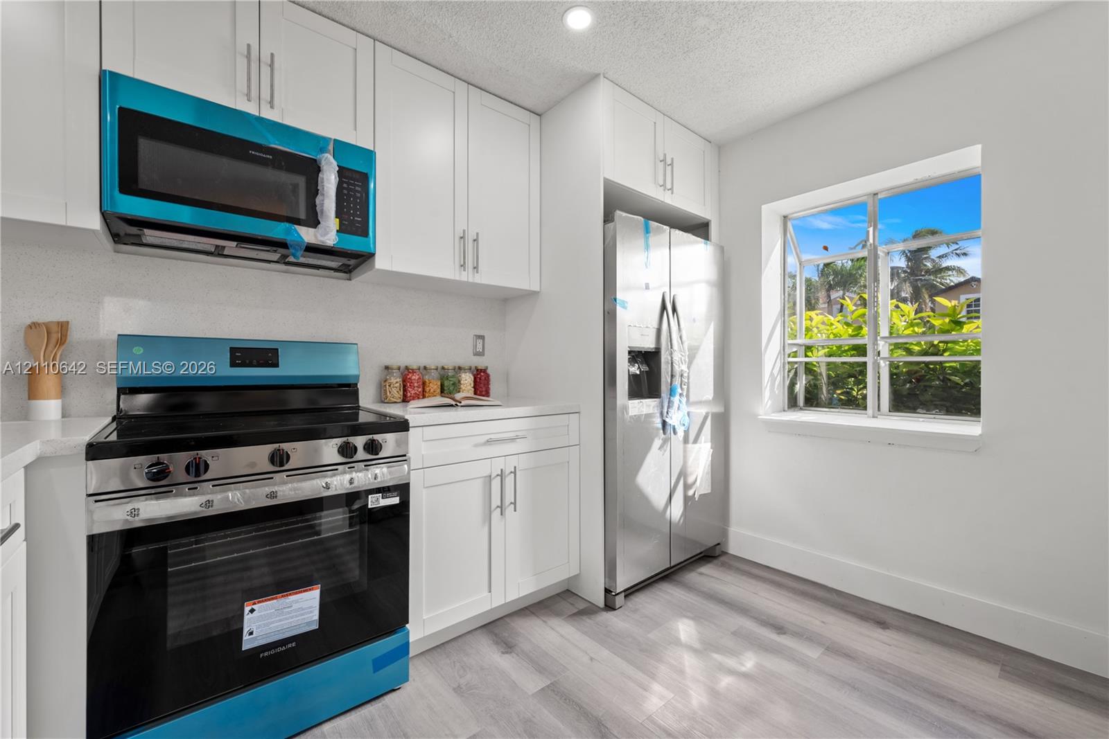Kitchen featuring white shaker-style cabinetry, wood-finish flooring, stainless steel side-by-side refrigerator, slide-in range with glass cooktop, and an over-the-range microwave Kitchen featuring white shaker-style cabinetry, wood-finish flooring, stainless steel side-by-side refrigerator, slide-in range with glass cooktop, and an over-the-range microwave