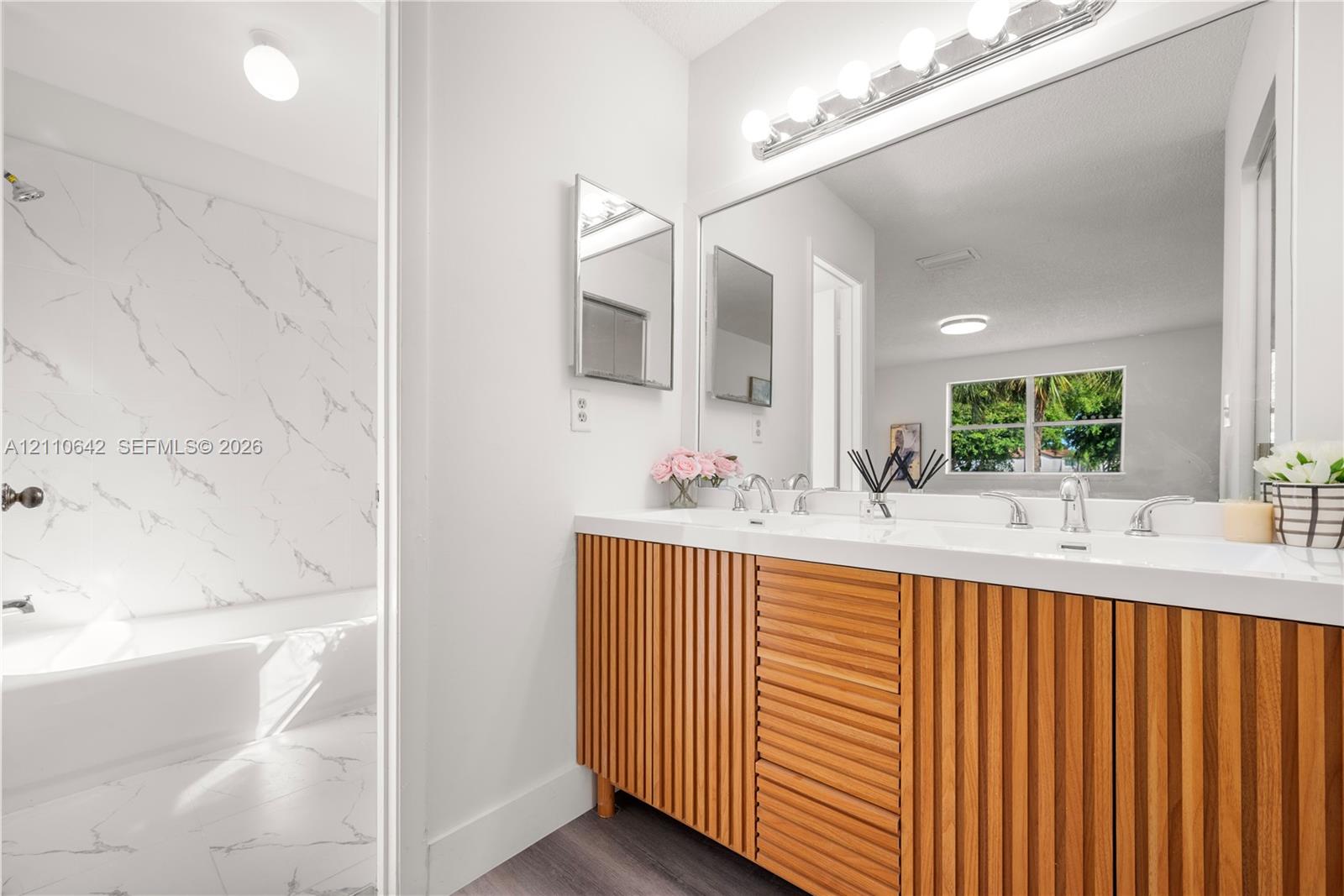 Double vanity with slatted wood-finish cabinetry, integrated rectangular sinks, expansive wall-to-wall mirror, and floor-to-ceiling tilework featuring stone-patterned wall panels