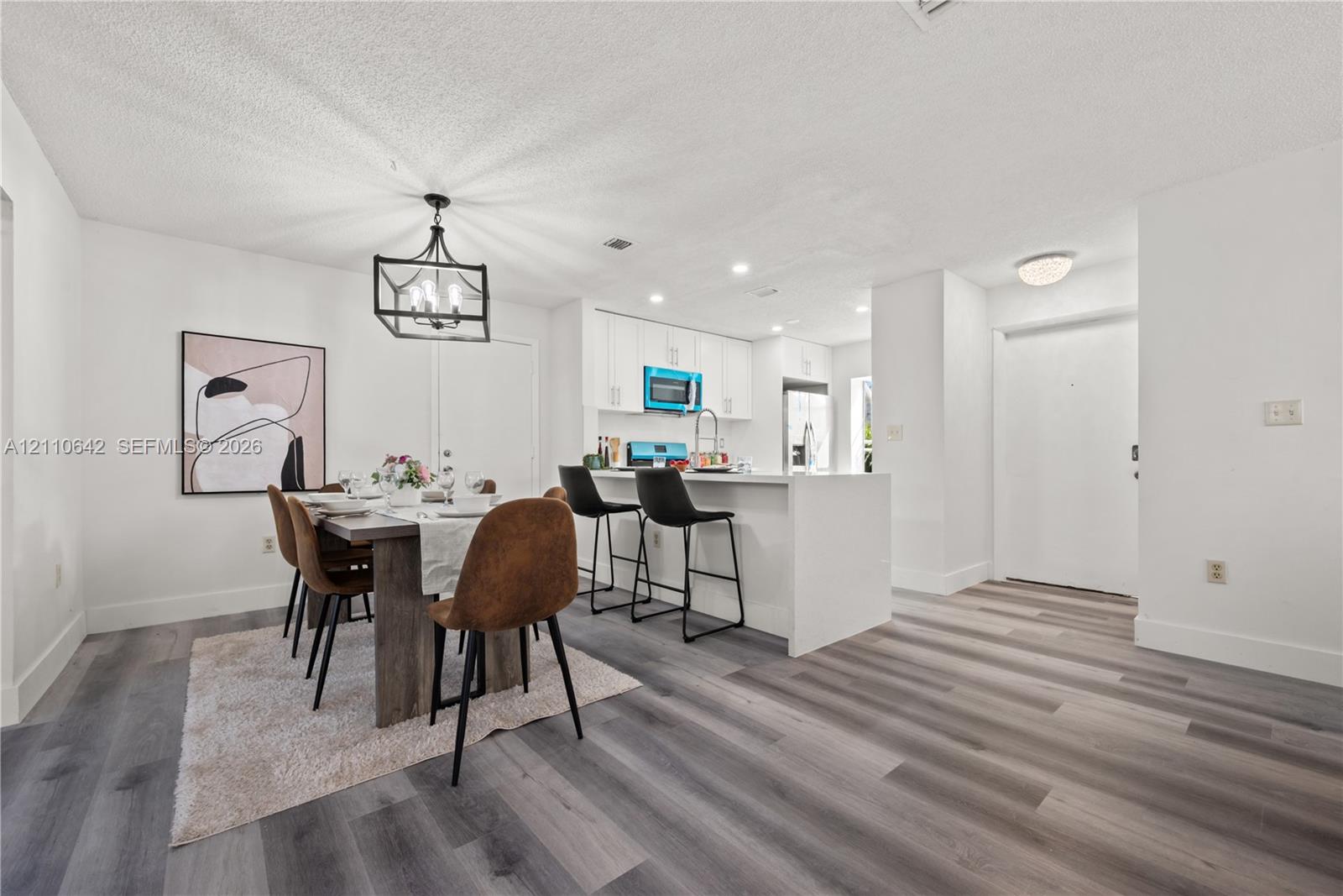 Kitchen featuring white cabinetry, an island with stone-surface countertop, and wood-finish flooring throughout the space, accented by a geometric metal chandelier Kitchen featuring white cabinetry, an island with stone-surface countertop, and wood-finish flooring throughout the space, accented by a geometric metal chandelier