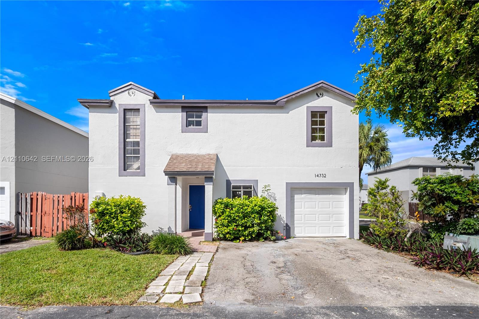 Two-story stucco exterior featuring a built-in single-car garage, defined entryway with a gabled porch cover, stone-paver walkway, and mature landscaping Two-story stucco exterior featuring a built-in single-car garage, defined entryway with a gabled porch cover, stone-paver walkway, and mature landscaping