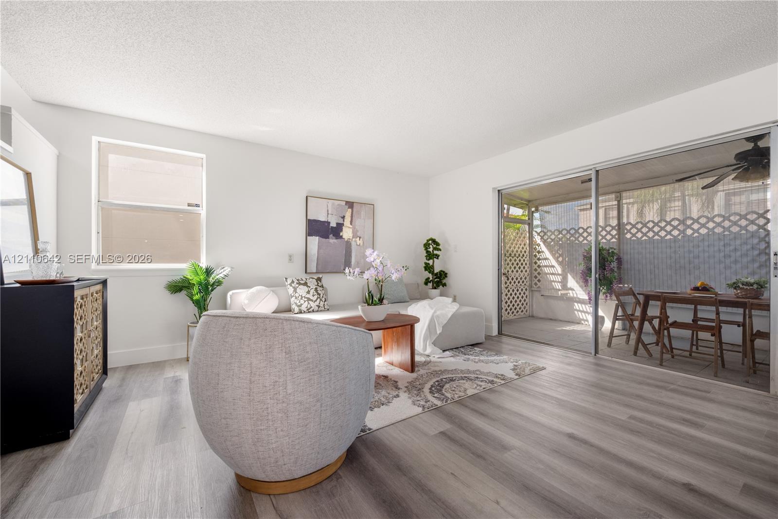 Living area featuring wood-finish flooring, a single-hung window, and glass sliding doors opening to a covered patio Living area featuring wood-finish flooring, a single-hung window, and glass sliding doors opening to a covered patio