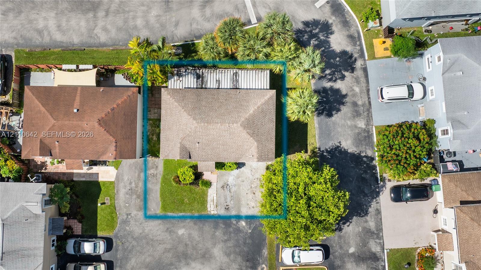 Aerial perspective featuring a hip-roof structure, concrete driveway, and landscaped front lawn with mature palms
