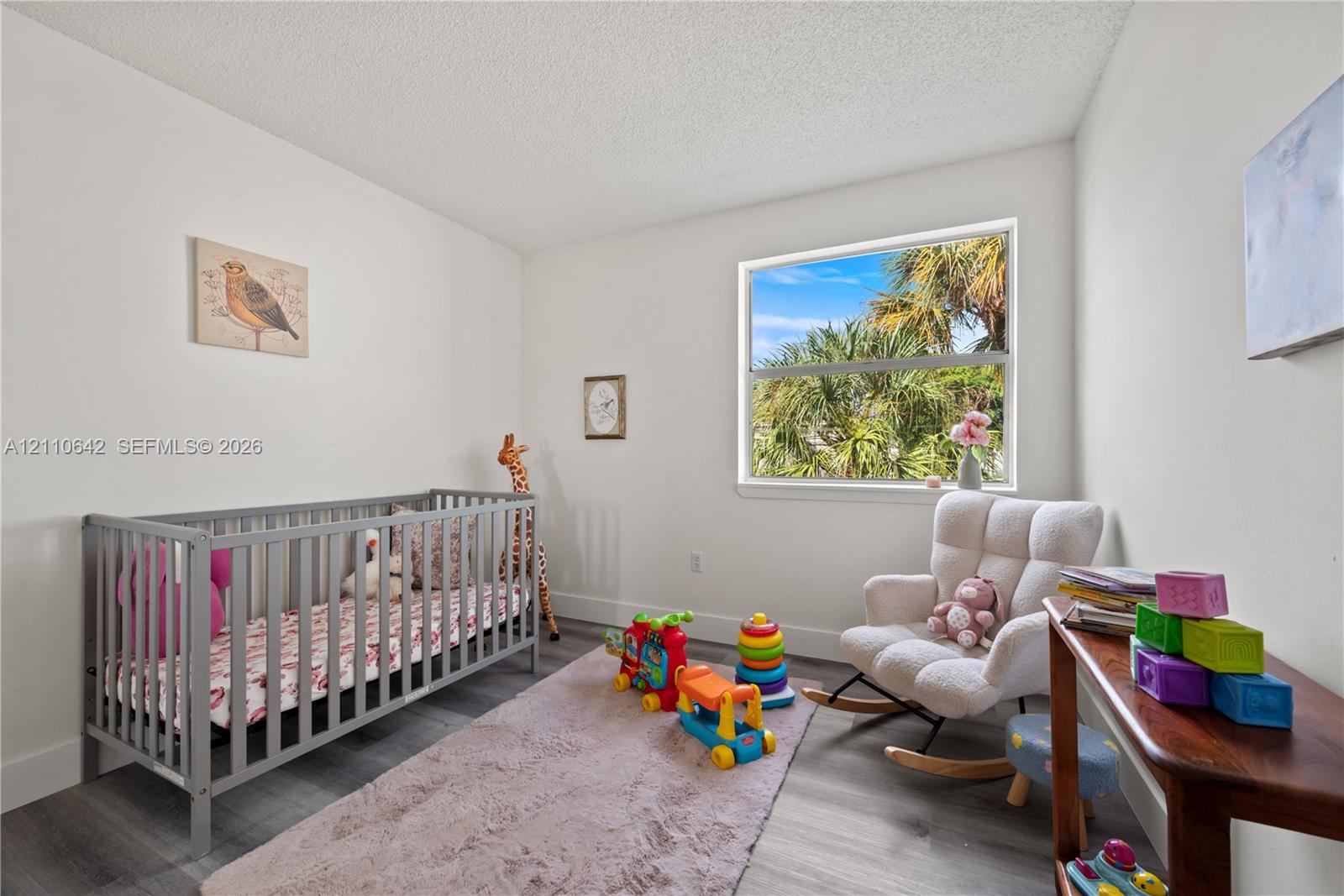 Neutral wall finishes, wood-finish flooring, and a single-pane window with tropical landscape scenery