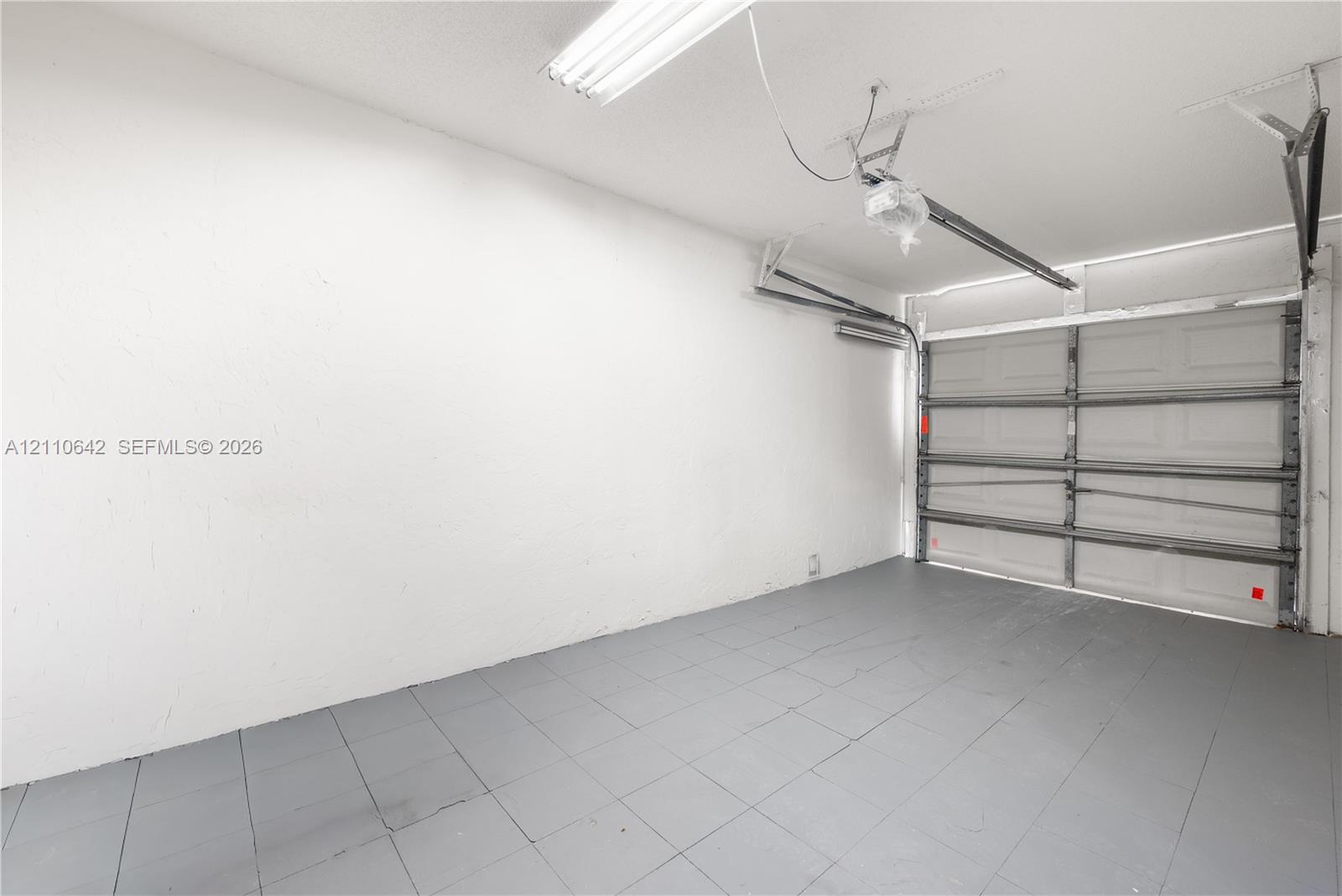 Garage interior featuring a sectional overhead door, painted flooring, textured walls, and a ceiling-mounted lighting fixture