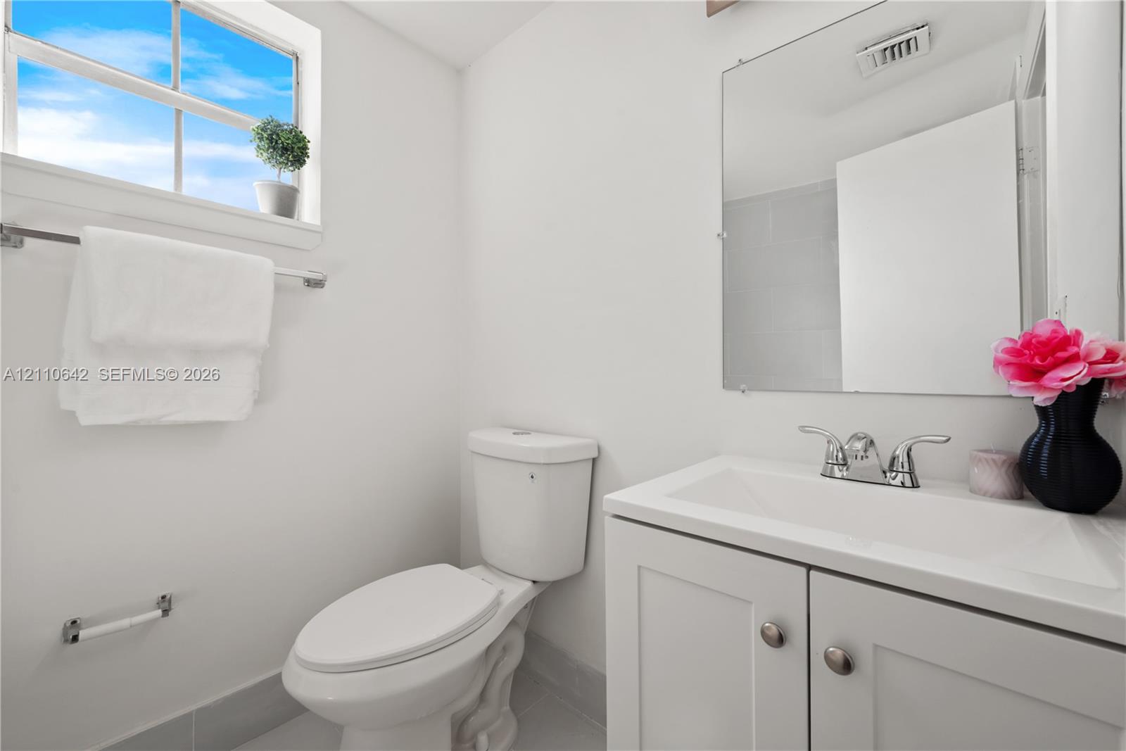 White vanity with an integrated sink and chrome hardware, framed mirror, and a multi-pane window