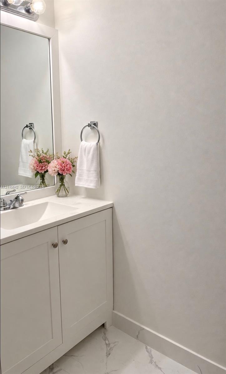 White vanity cabinet with a stone-composite countertop, integrated rectangular sink, chrome-finished faucet, framed mirror, and polished stone-finish floor tile