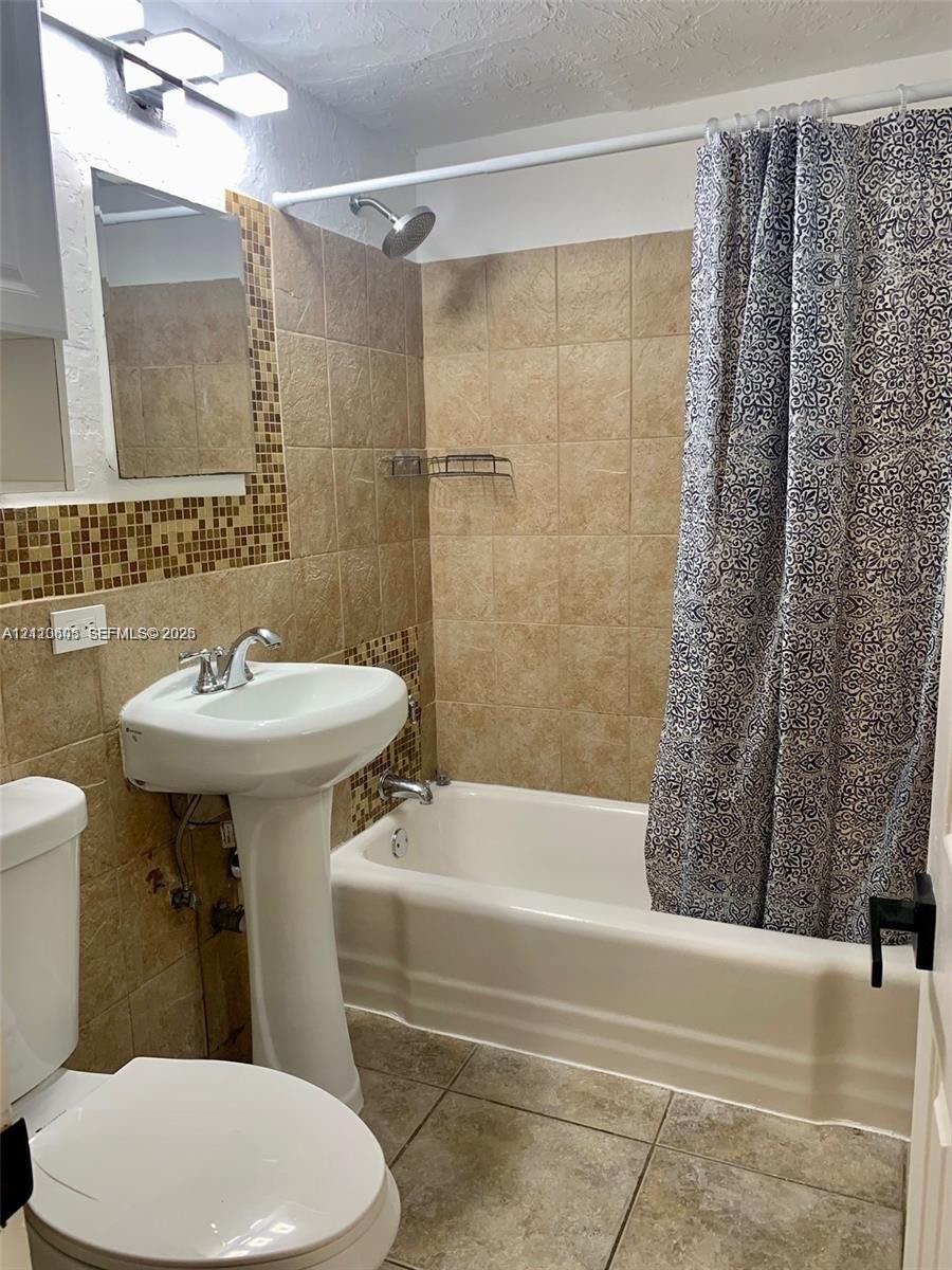 Pedestal sink with chrome faucet, shower-tub combination, ceramic wall tile surround with mosaic tile accents, and tiled flooring
