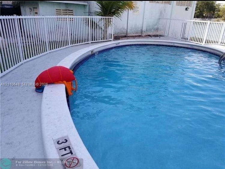 Circular swimming pool featuring a concrete deck and white aluminum perimeter fencing Circular swimming pool featuring a concrete deck and white aluminum perimeter fencing