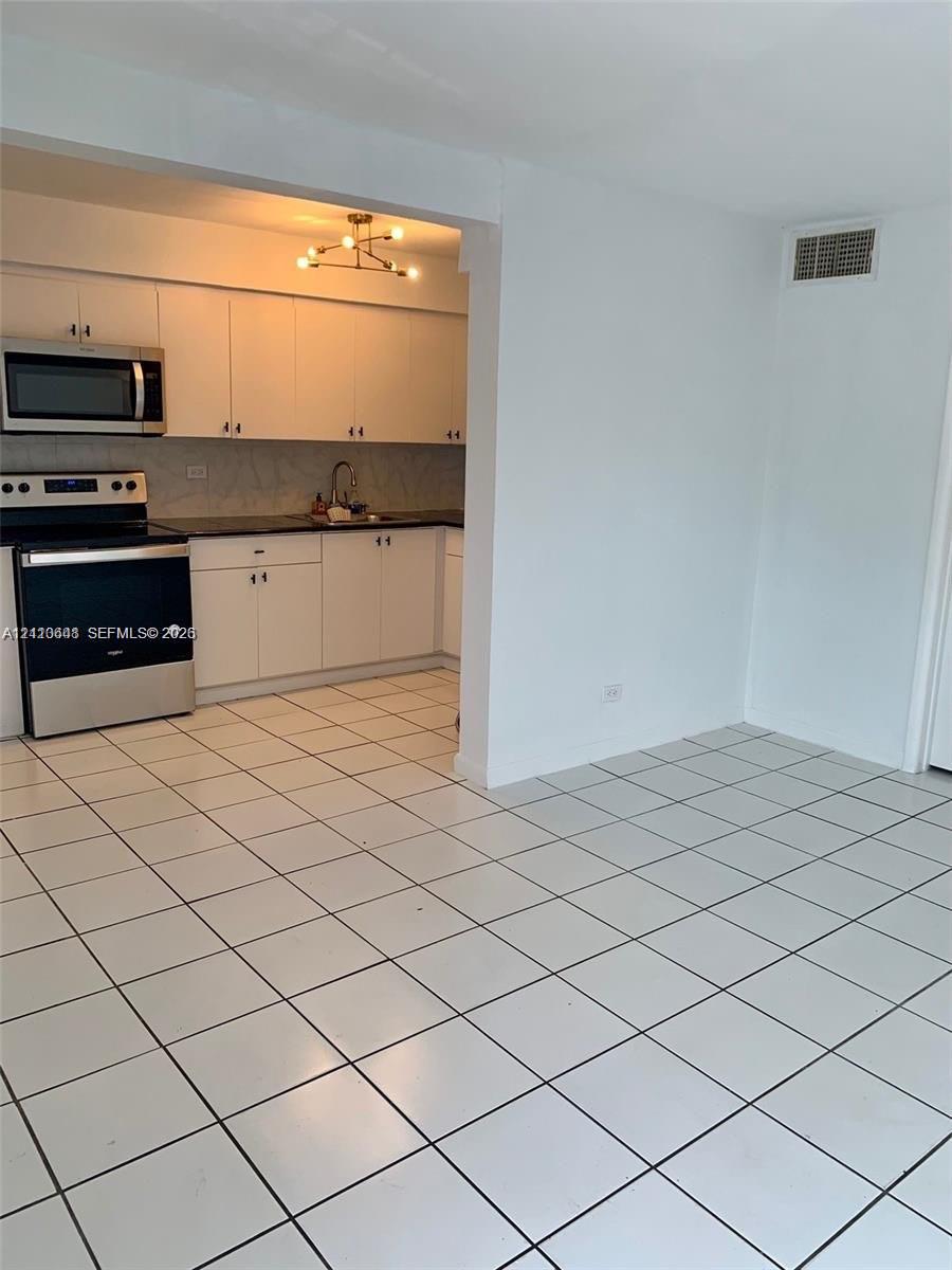 Kitchen featuring white cabinetry, dark countertops, a stainless steel range and microwave, and ceramic tile flooring