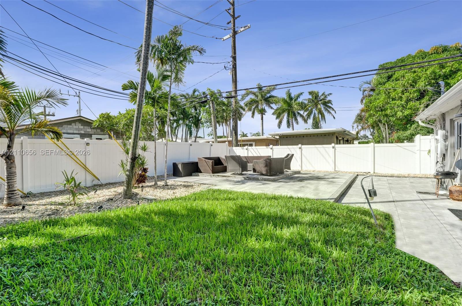 Backyard featuring a paved patio, manicured lawn, white vinyl perimeter fencing, and mature palm trees