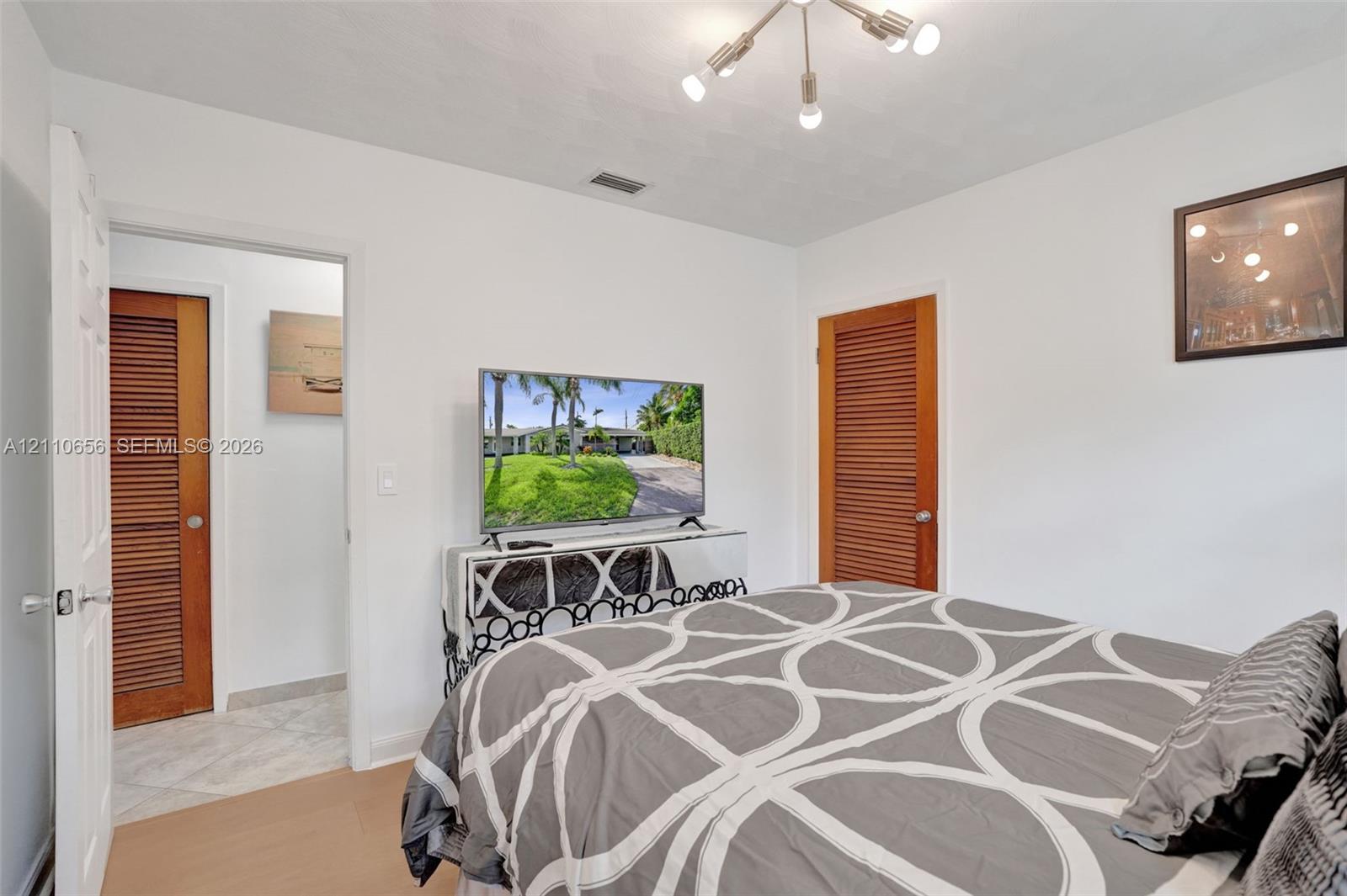 Neutral interior featuring wood-finish flooring, a multi-arm modern light fixture, and dual wood-tone louvered doors
